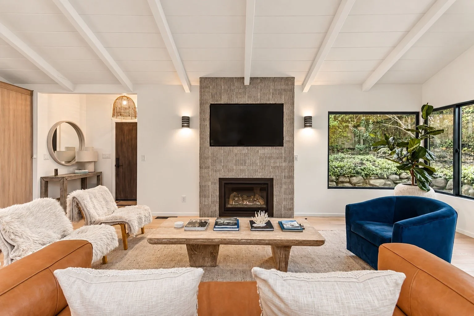 Carmel living room with a tiled fireplace, tan leather sofa, white lounge chairs, and a blue accent chair.