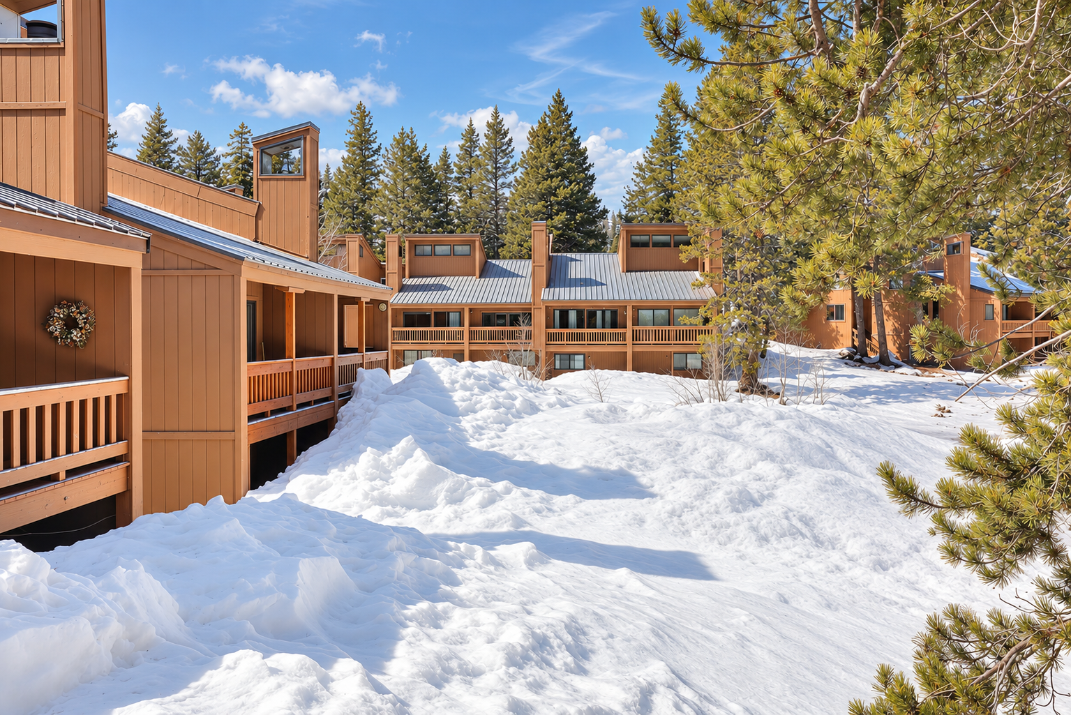 Snow-covered Bear Valley condominiums with brown wood siding, balconies, and pine trees under a blue sky