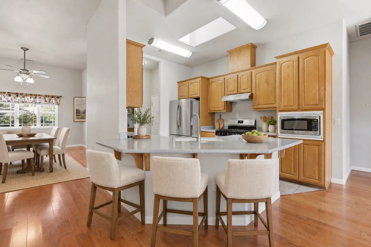 Virtually staged Oakdale kitchen and dining area with oak cabinets and upholstered counter stools.
