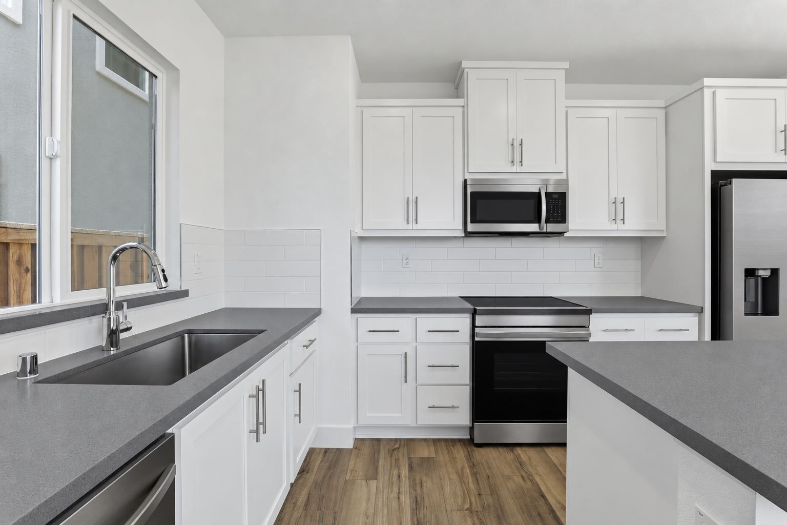 Modern kitchen with white cabinets, gray countertops, stainless steel appliances, and wood flooring.