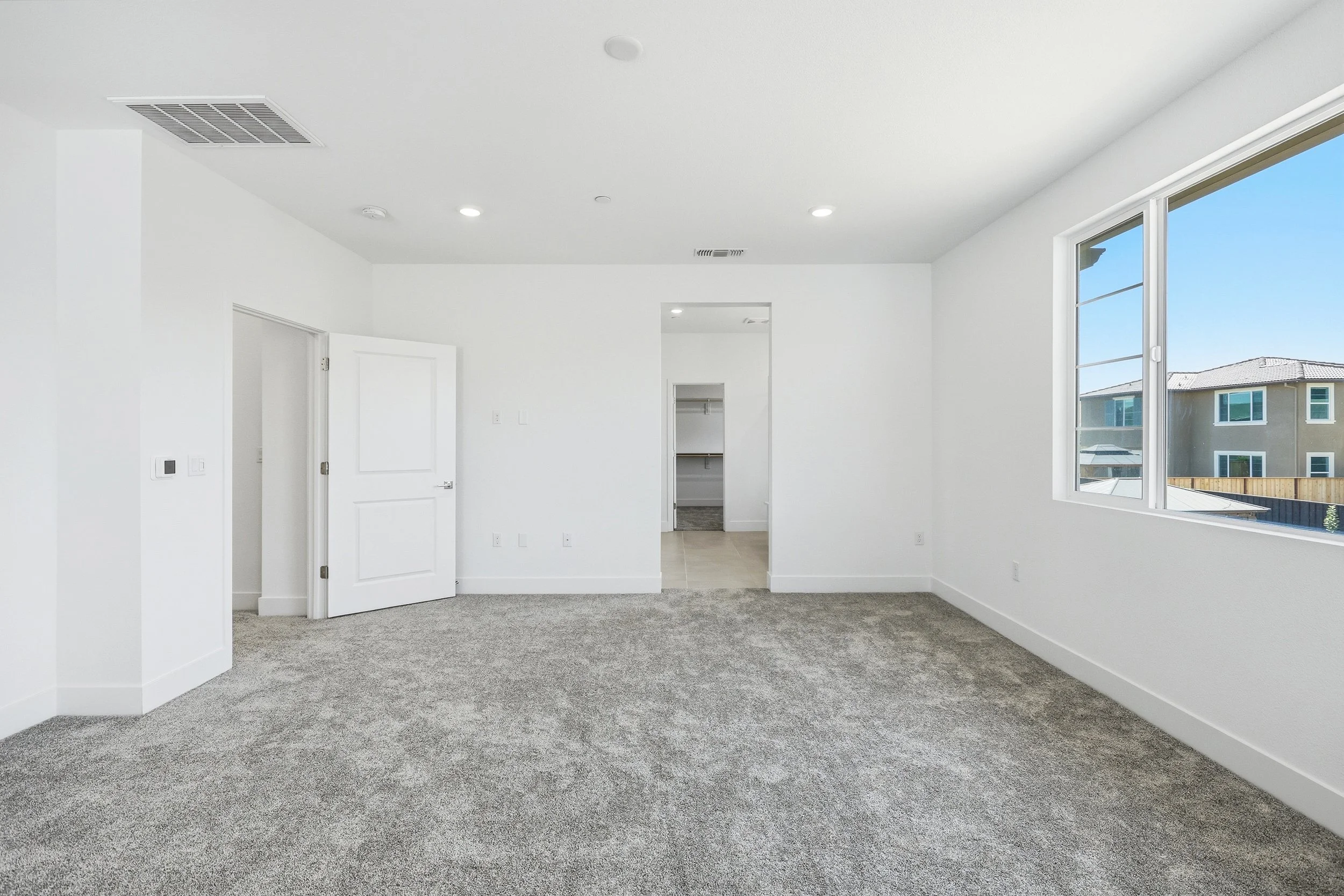 Empty carpeted bedroom with white walls and recessed lighting.
