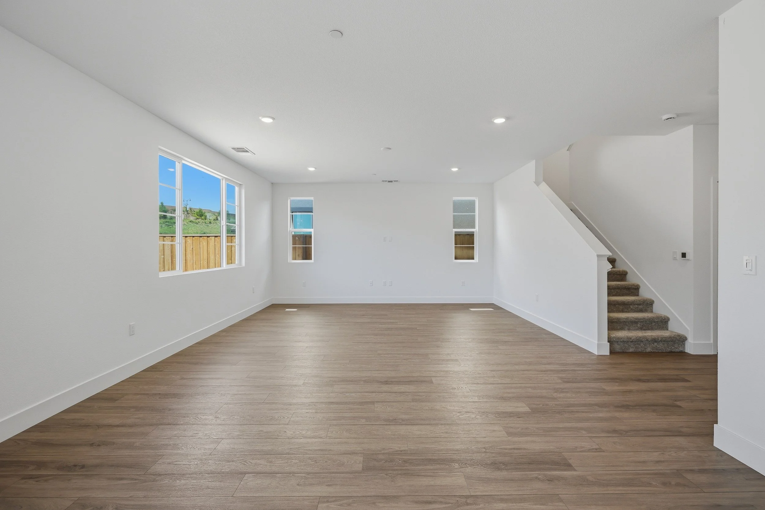 Open living area with wood flooring, wide windows, and a staircase.