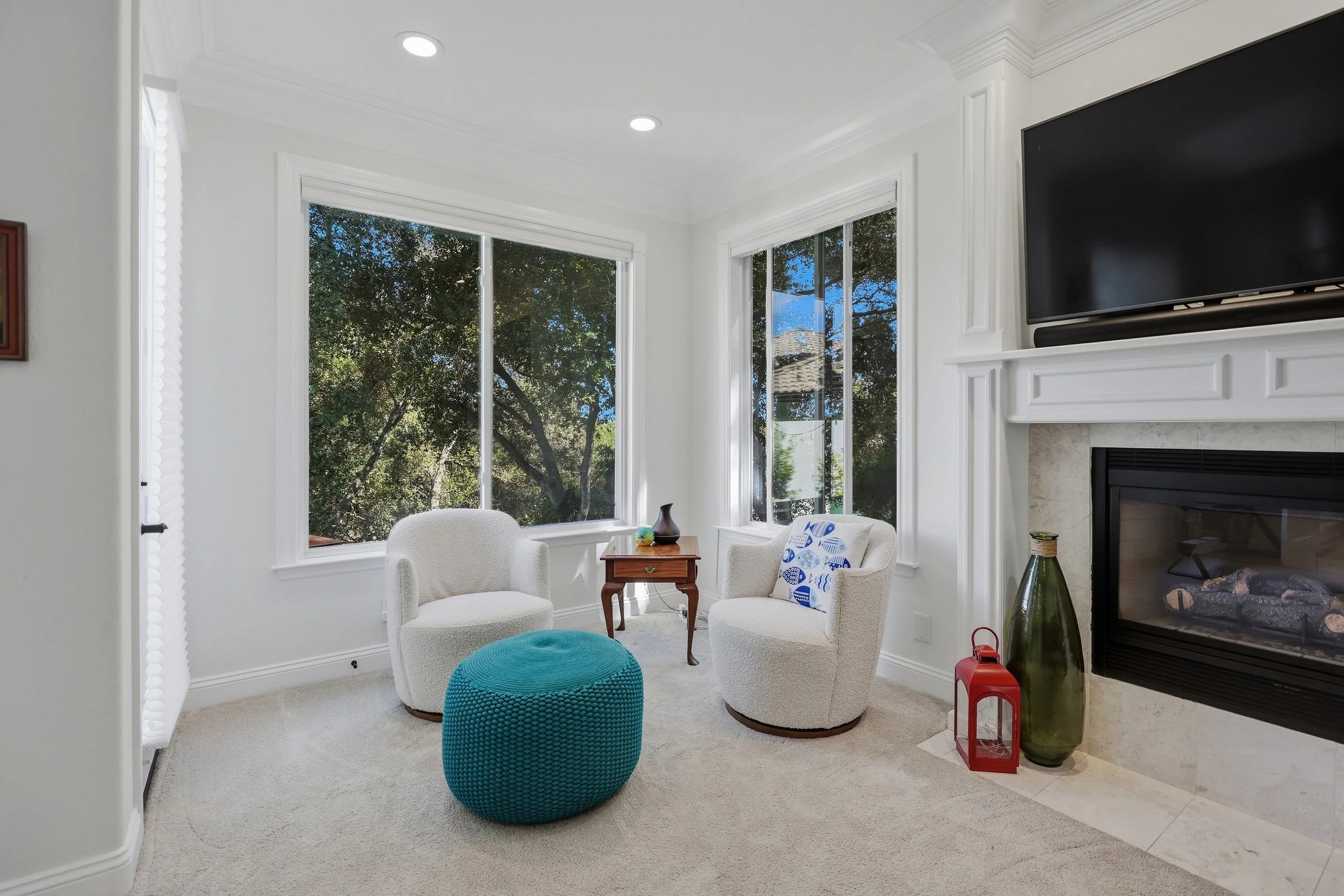 Bright home office with white desk, large windows, and a teal ottoman.