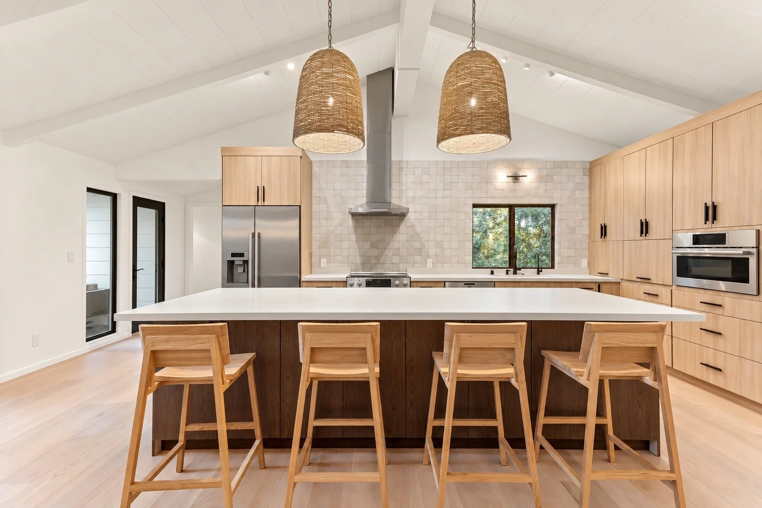 Carmel kitchen with natural wood cabinetry, a white island, four wooden stools, and woven pendant lights.