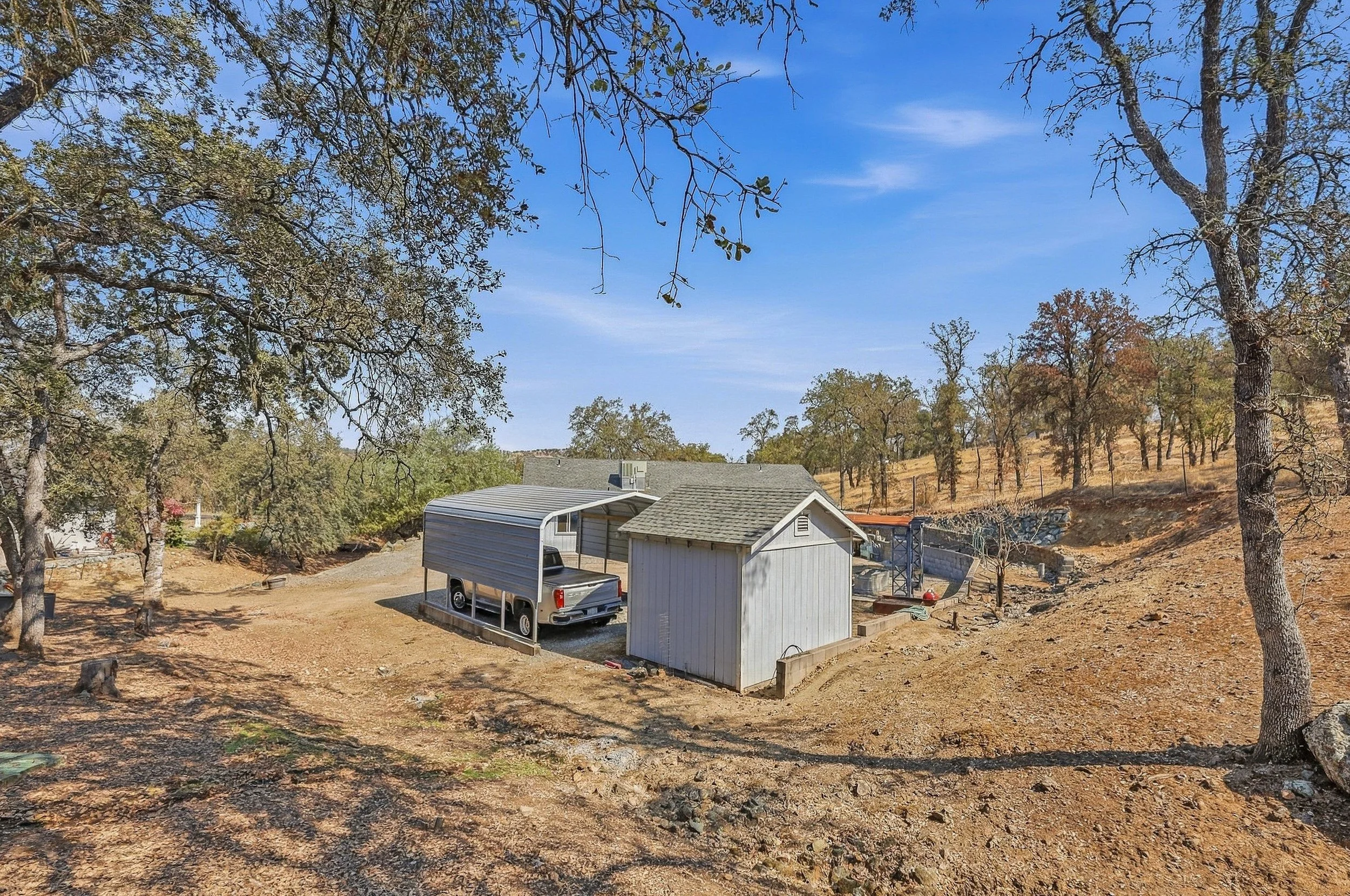 Detached outbuilding on a rural property surrounded by dry grass and trees.
