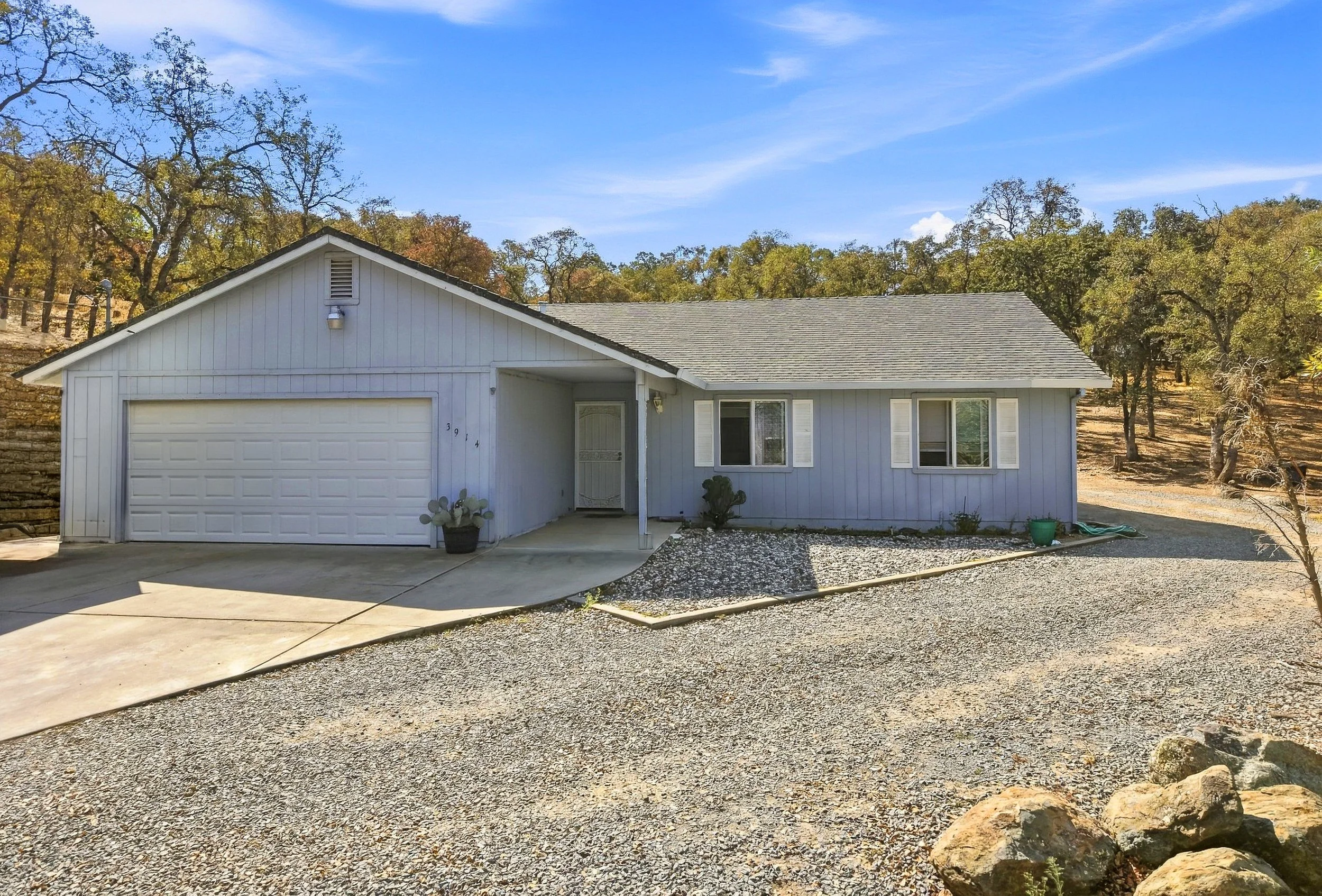 Single-story Valley Springs home with garage, gravel driveway, and surrounding oak trees.