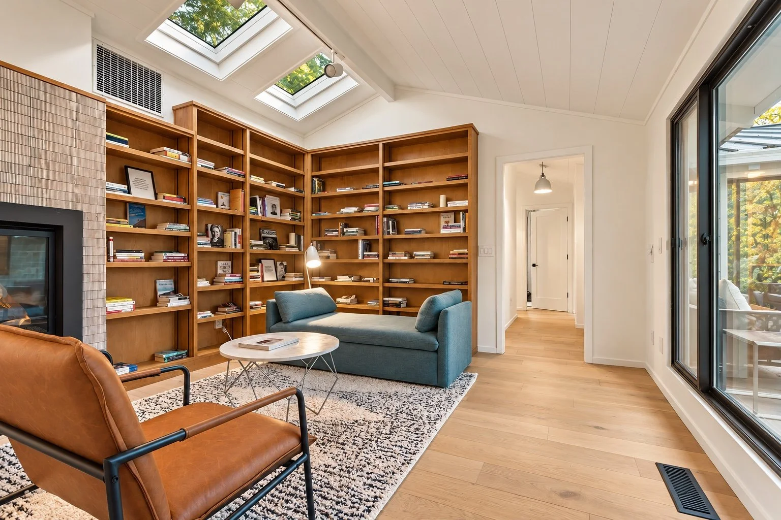 Carmel reading room with built-in wood bookshelves, a blue chaise, skylights, and glass doors to the courtyard.