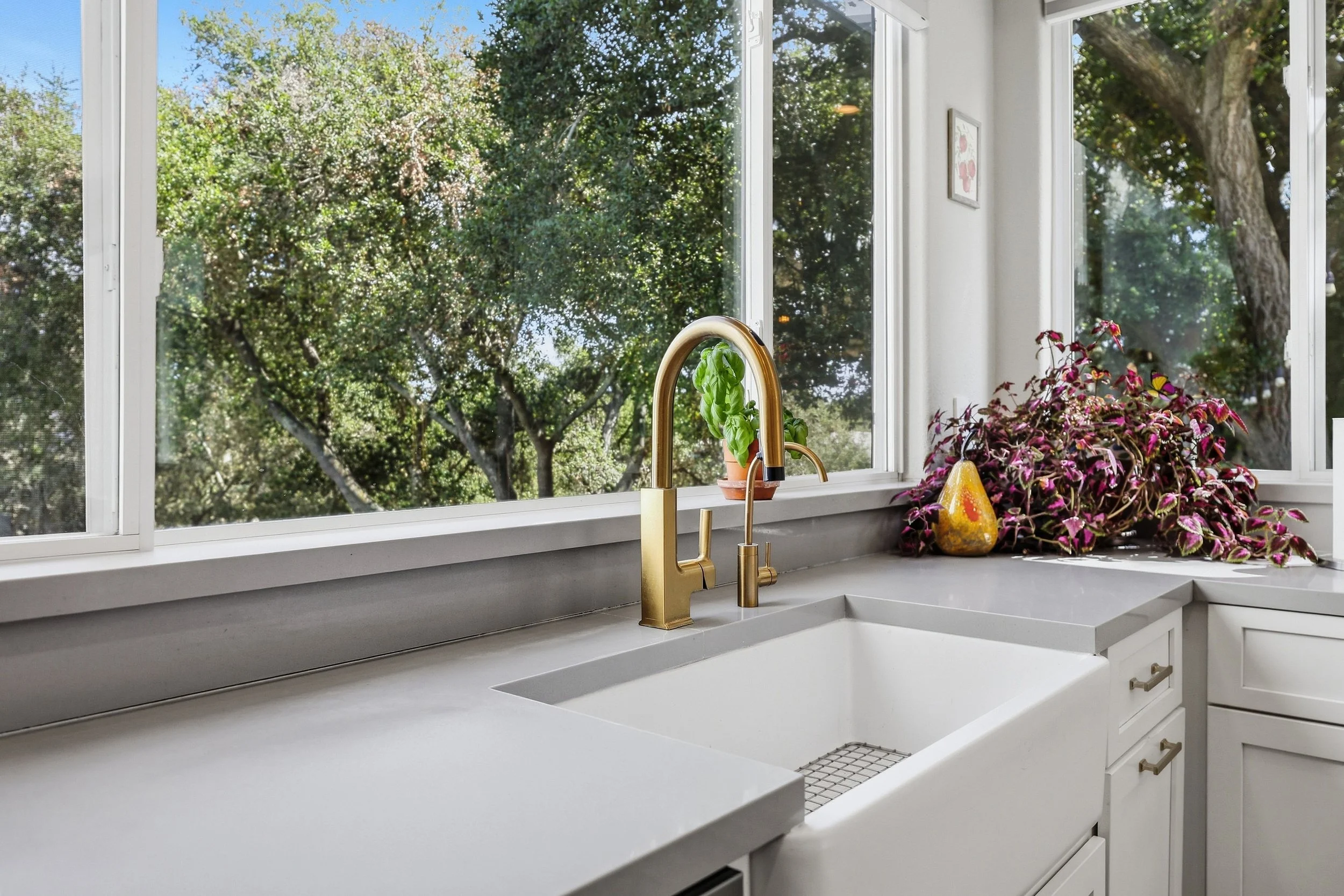 Kitchen sink and gold faucet below a window overlooking trees.