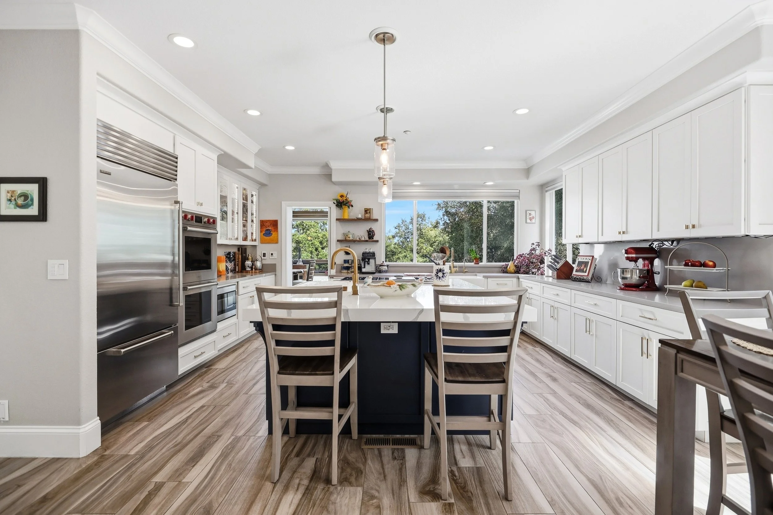 Kitchen with a large island, bar stools, white cabinetry, and recessed lighting.