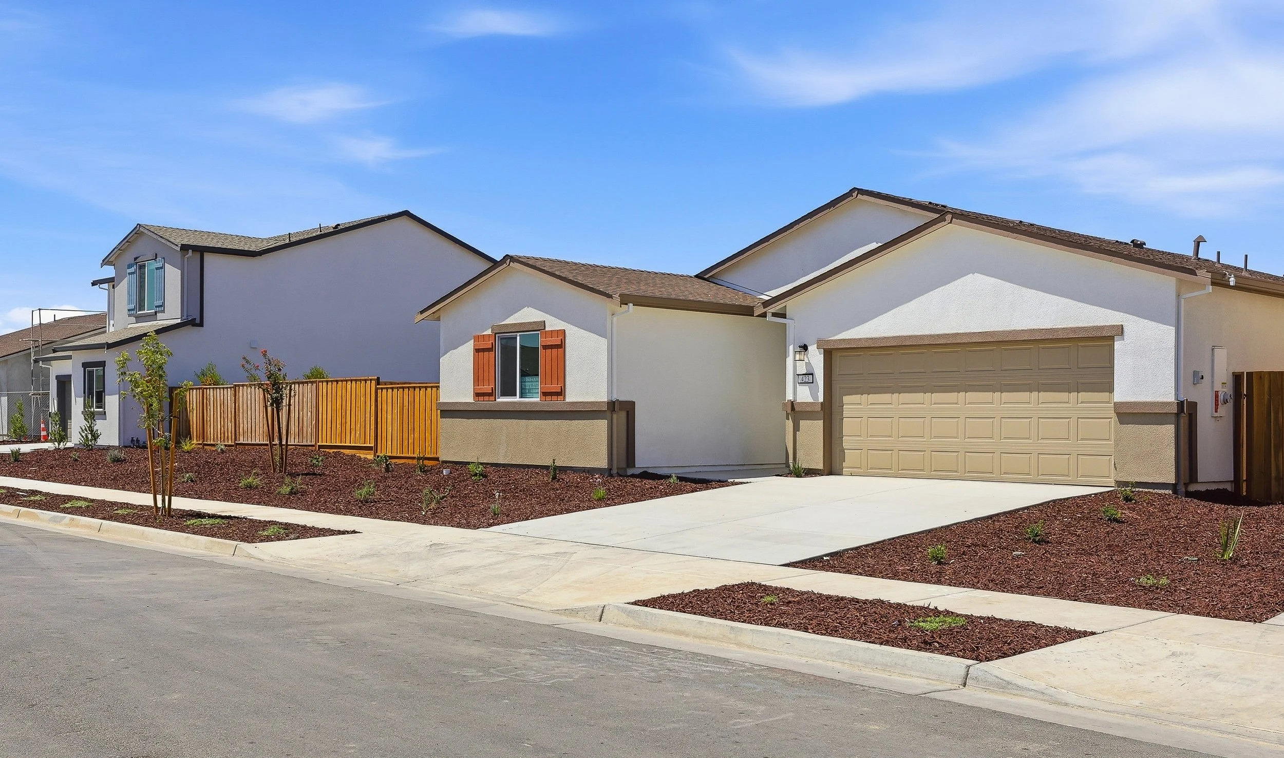 A row of modern suburban houses with white stucco exteriors, brown roofs, and neatly landscaped front yards under a blue sky.
