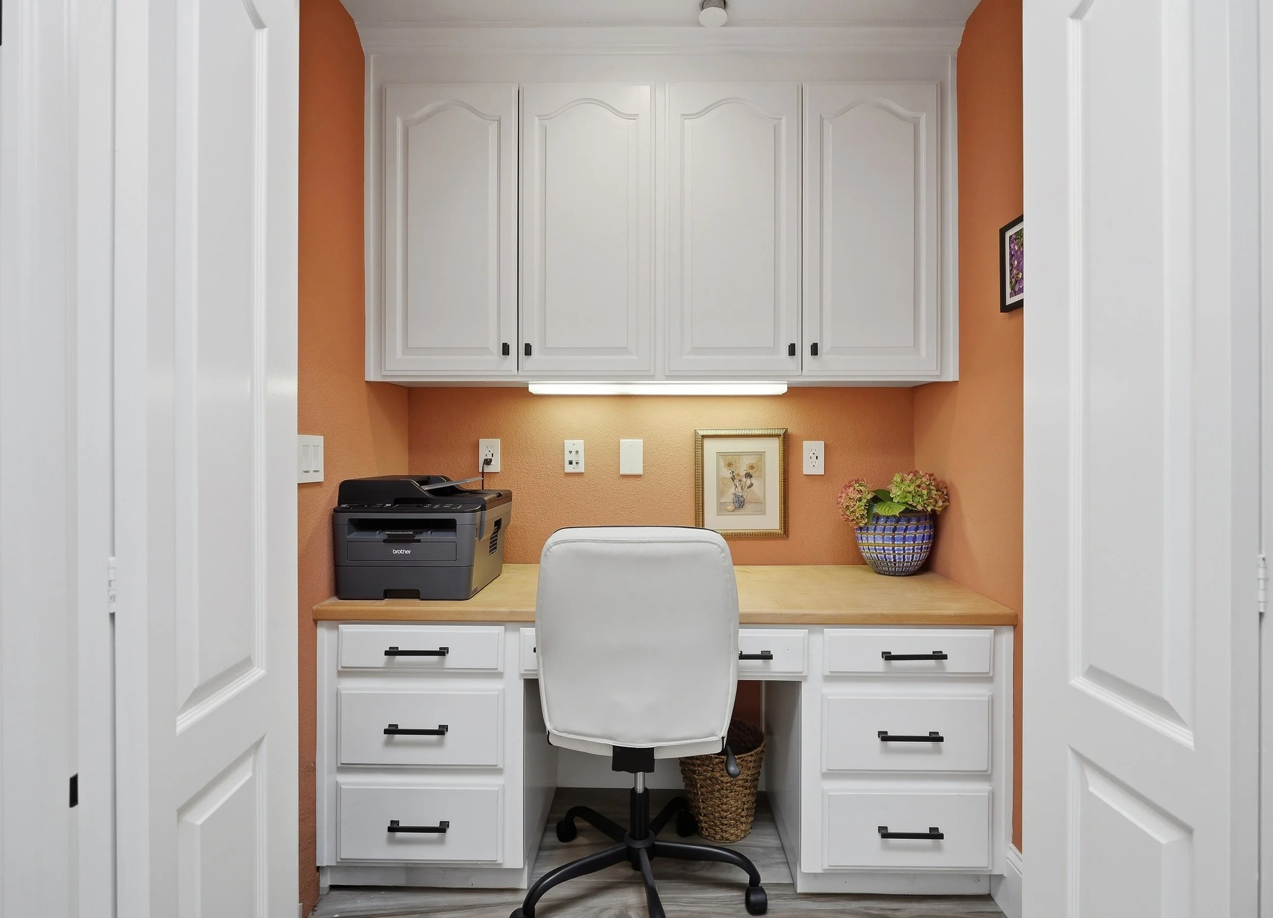 Built-in desk nook with white drawers, cabinets, and an office chair.