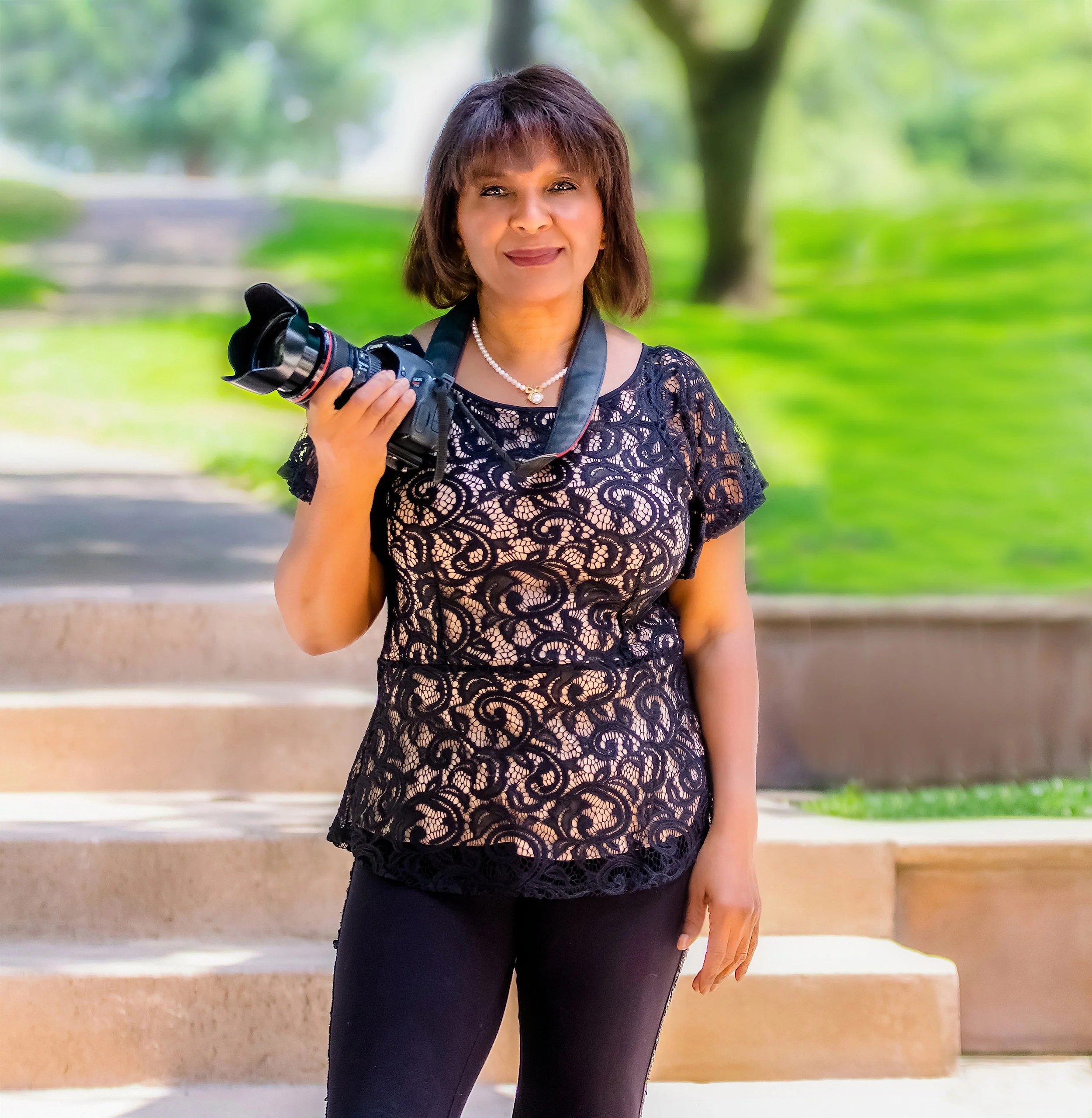 Carole Carnie holding a professional camera outdoors in a green park.