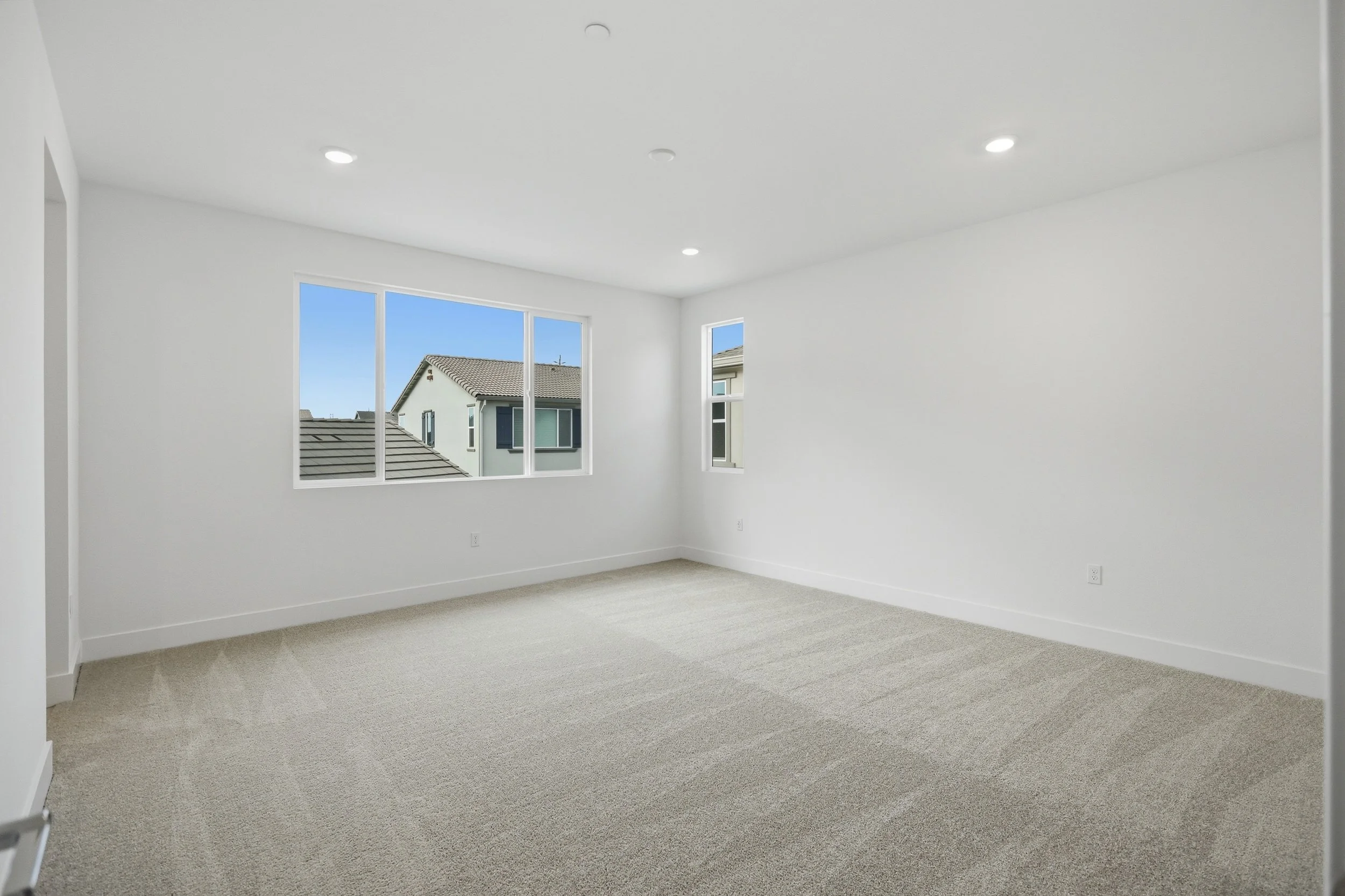 Empty carpeted room with white walls and large windows.