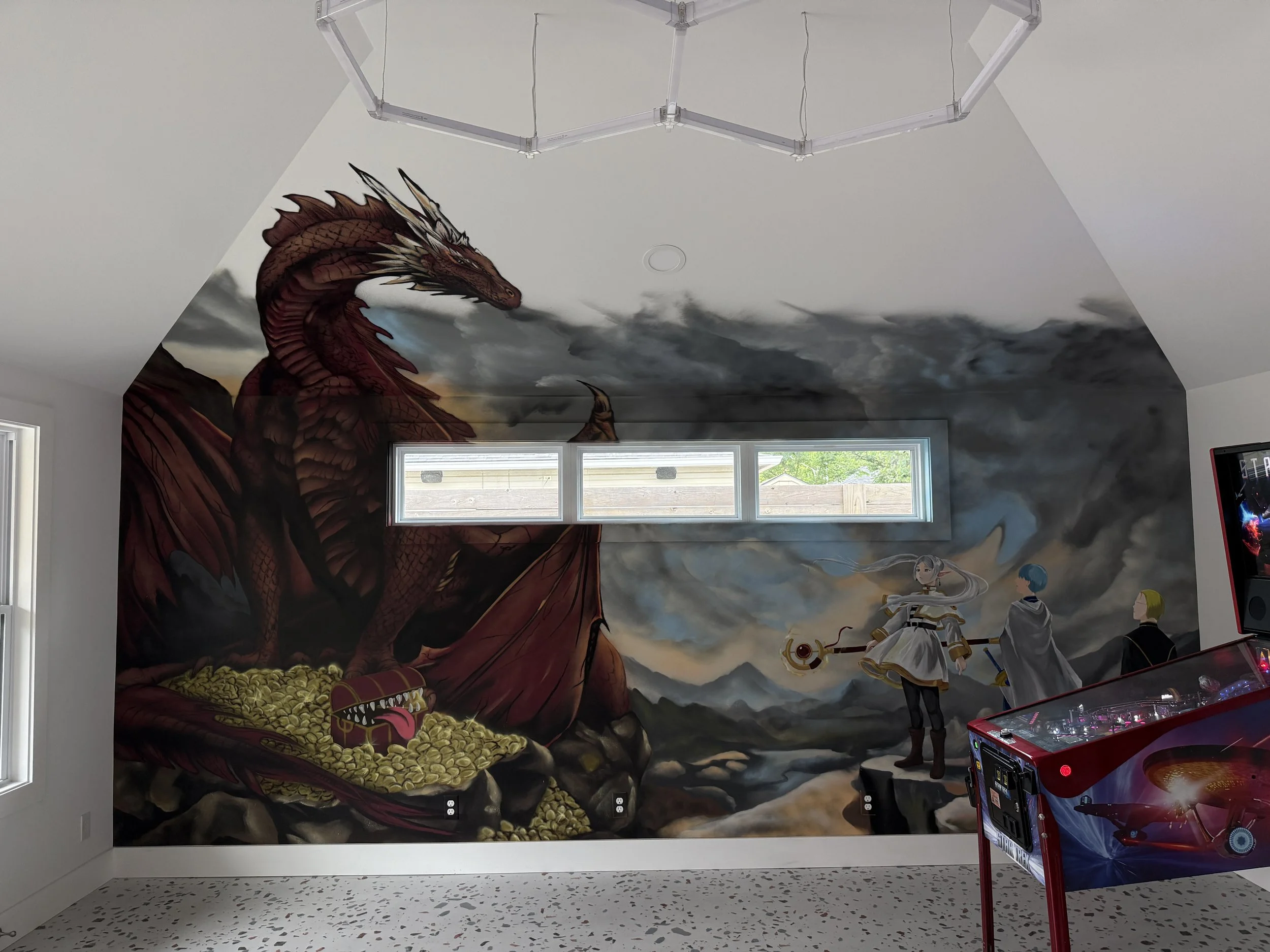 Created for a residential pinball game room, this Frieren inspired mural brought together the main characters, a shapeshifter treasure box, mountain scenery, and a large dragon extending beyond the wall through forced perspective. Painted with aeroso