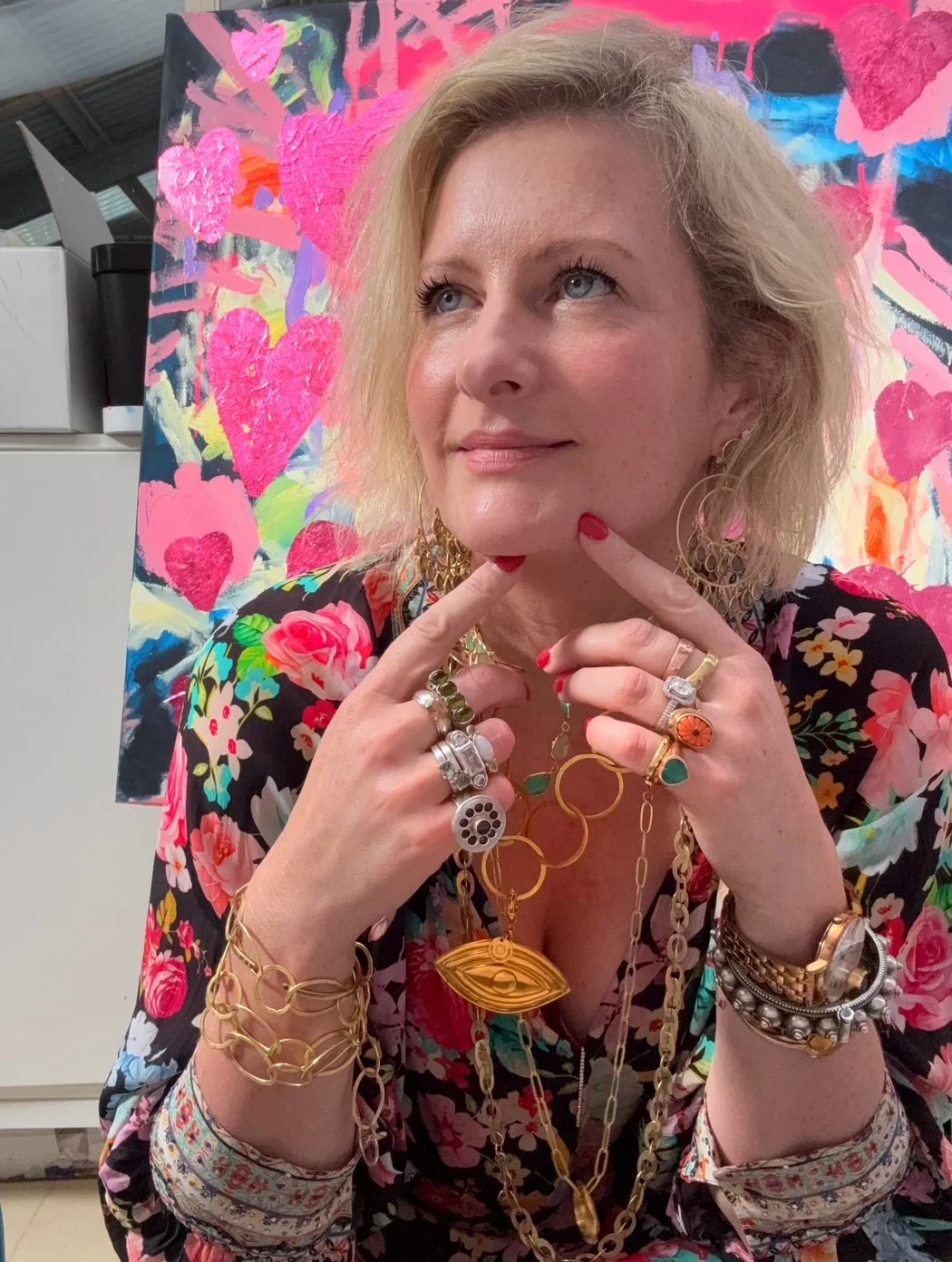 Young blonde Australian female artist Louisa de Haas is wearing a colourful silk floral dress and is dripping in gold and brass gemstone jewellery.