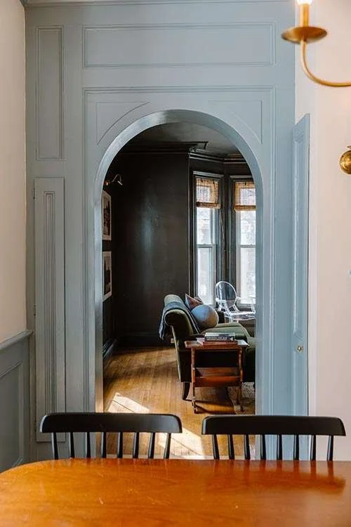 Ipswich Inn. A view through an archway into a cozy living room with a chair, a small table, and natural light from large windows. A restored historic home now an Inn.