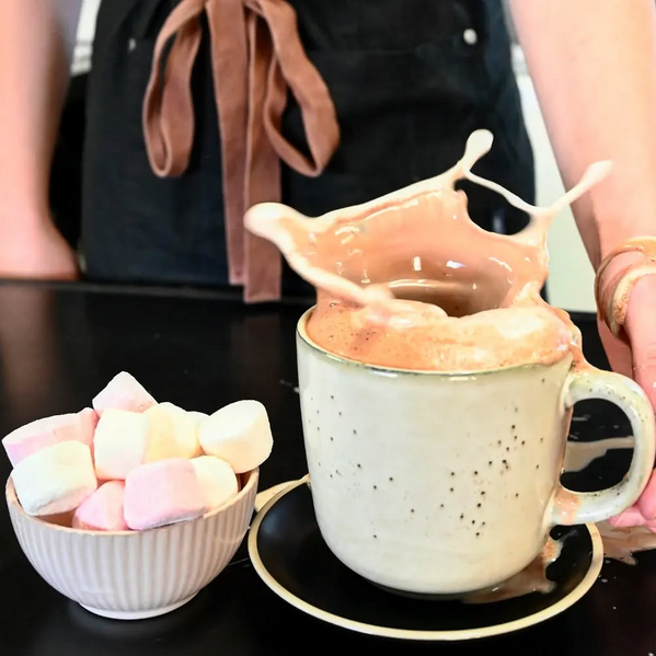 Large cup of hot chocolate making a splash next to a bowl of mashmallows