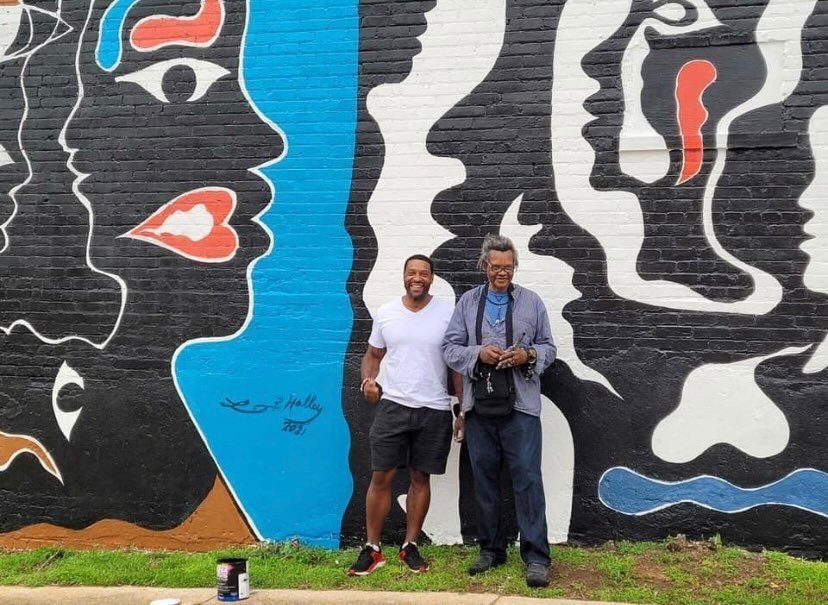 Lonnie Holley with his son Zeke in front of  the mural titled "Born Into Colors" and "Black in the Midst of the Red, White and Blue" (2021)