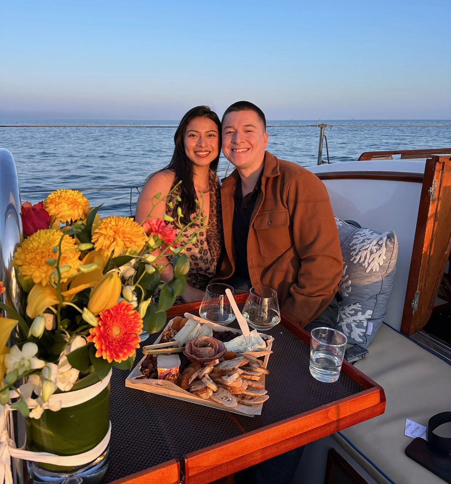 Couple celebrating aboard Kelpie with flowers, wine and a gourmet picnic platter during a private Santa Barbara sail.