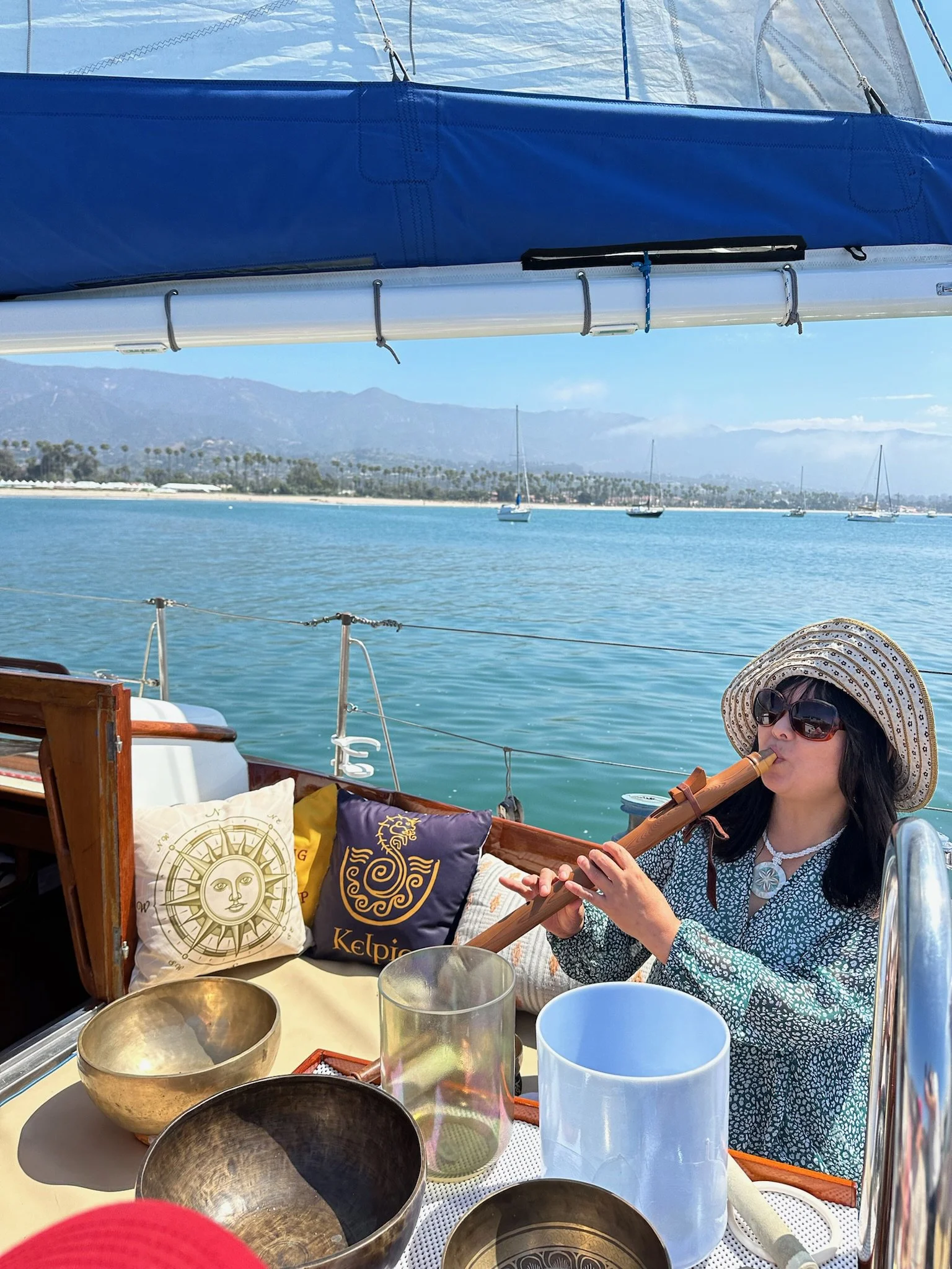Sound Practitioner playing flute with singing bowls aboard yacht Kelpie during a private Sound Bath Sail in Santa Barbara.