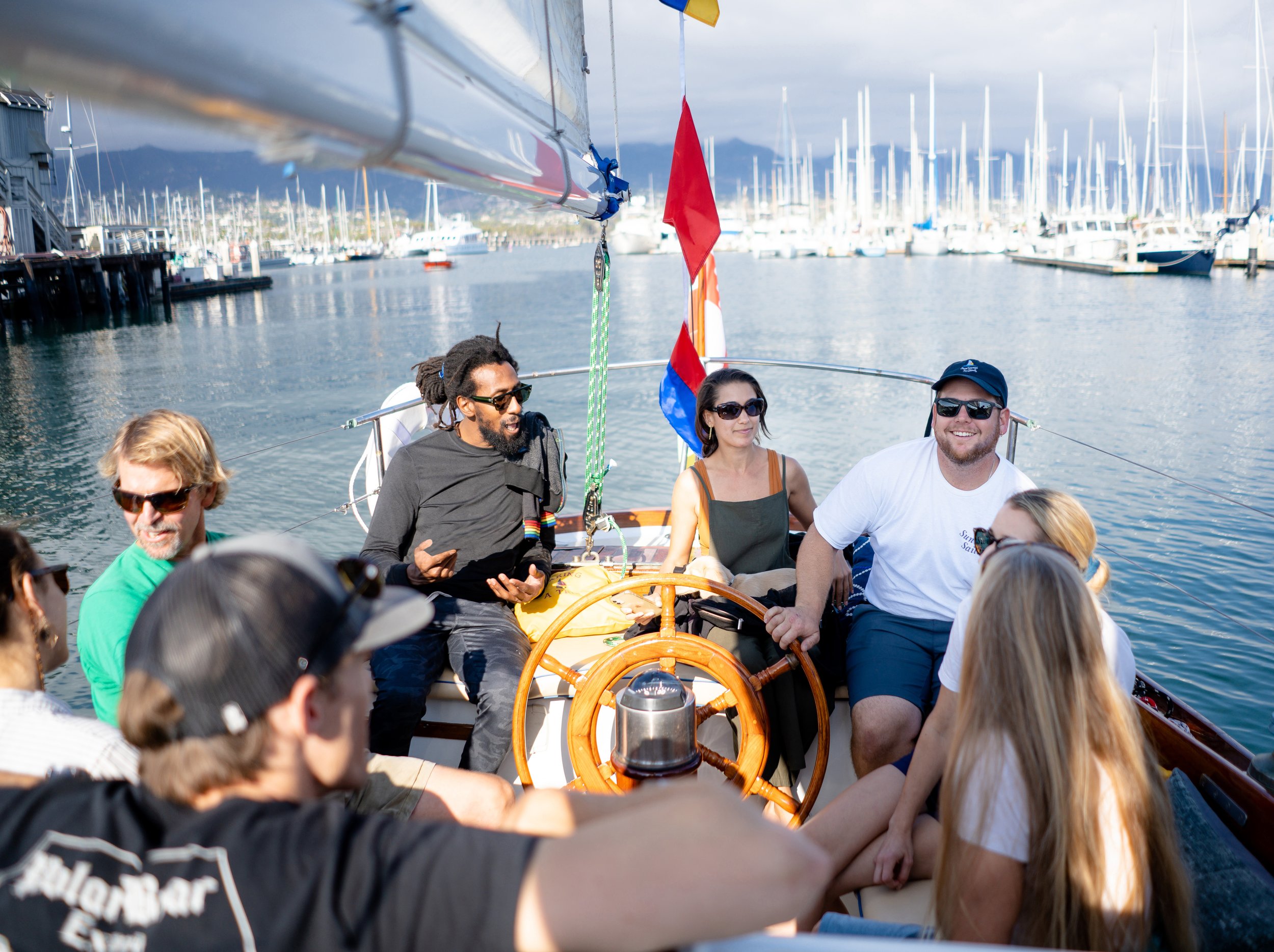 Guests relaxing around the wooden helm aboard Kelpie during a private Santa Barbara Harbor cruise.
