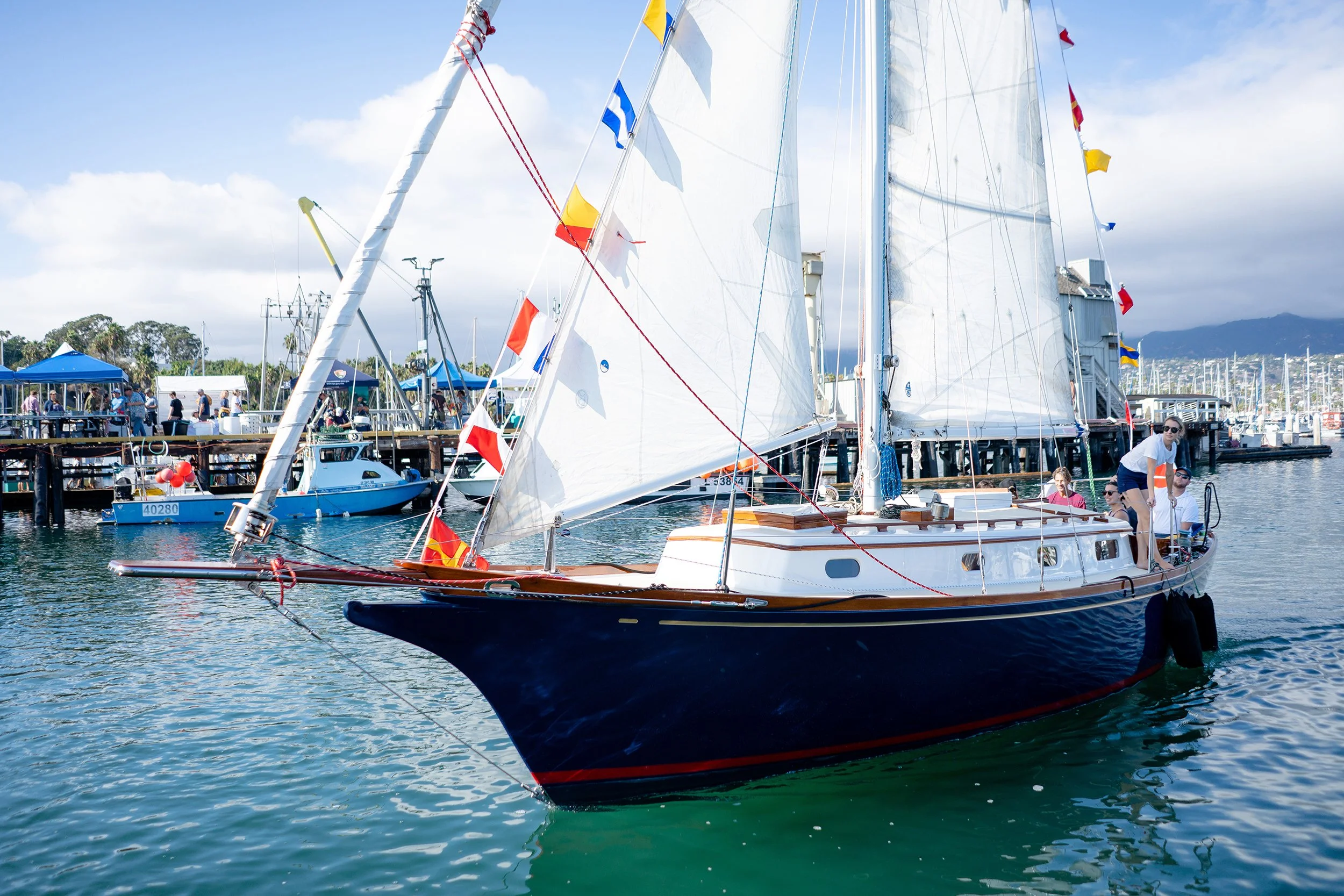 Classic yacht Kelpie sailing near the Santa Barbara waterfront with colorful signal flags flying.