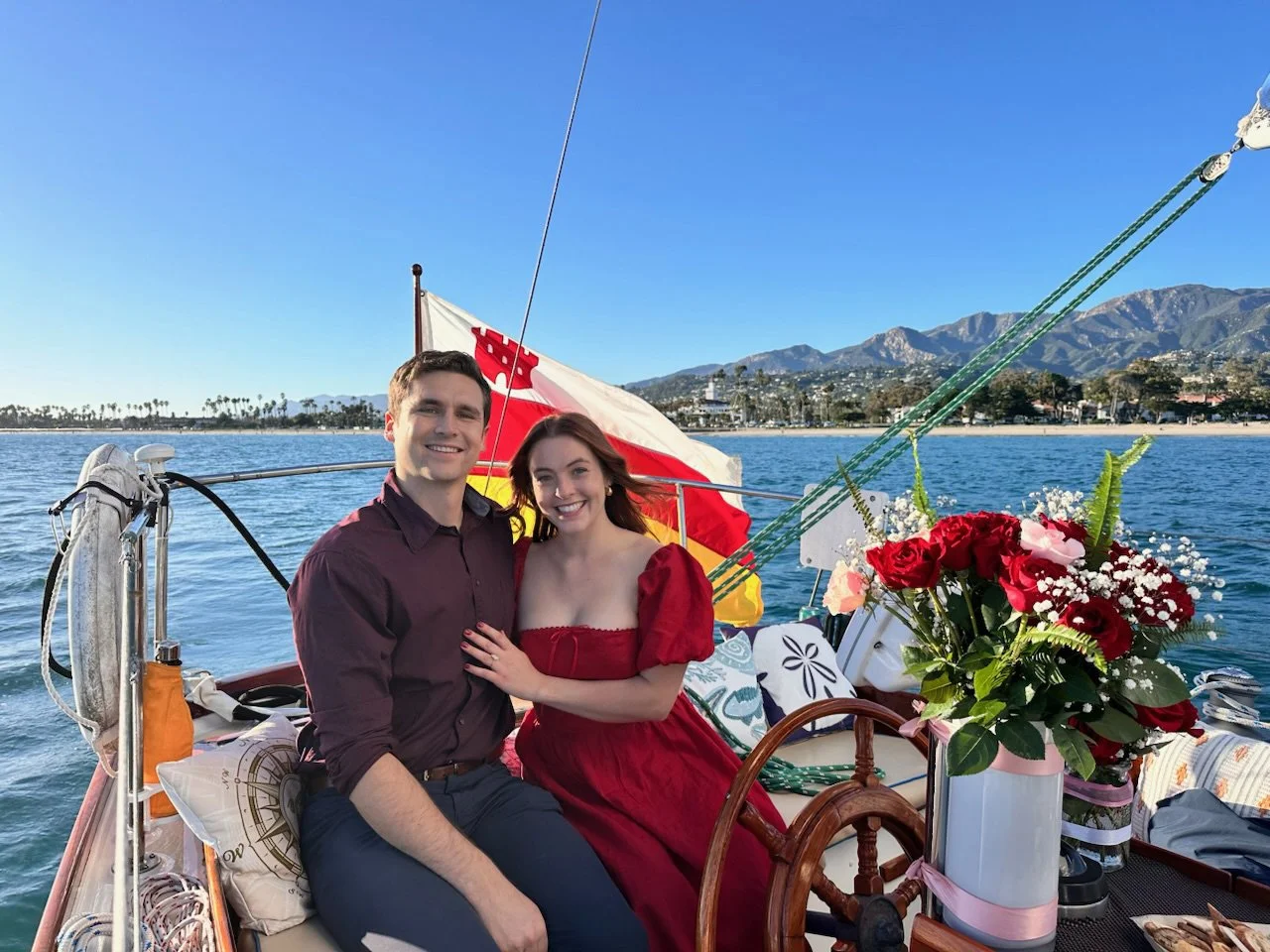 Couple seated beside the helm with flowers during a romantic sailing charter in Santa Barbara.