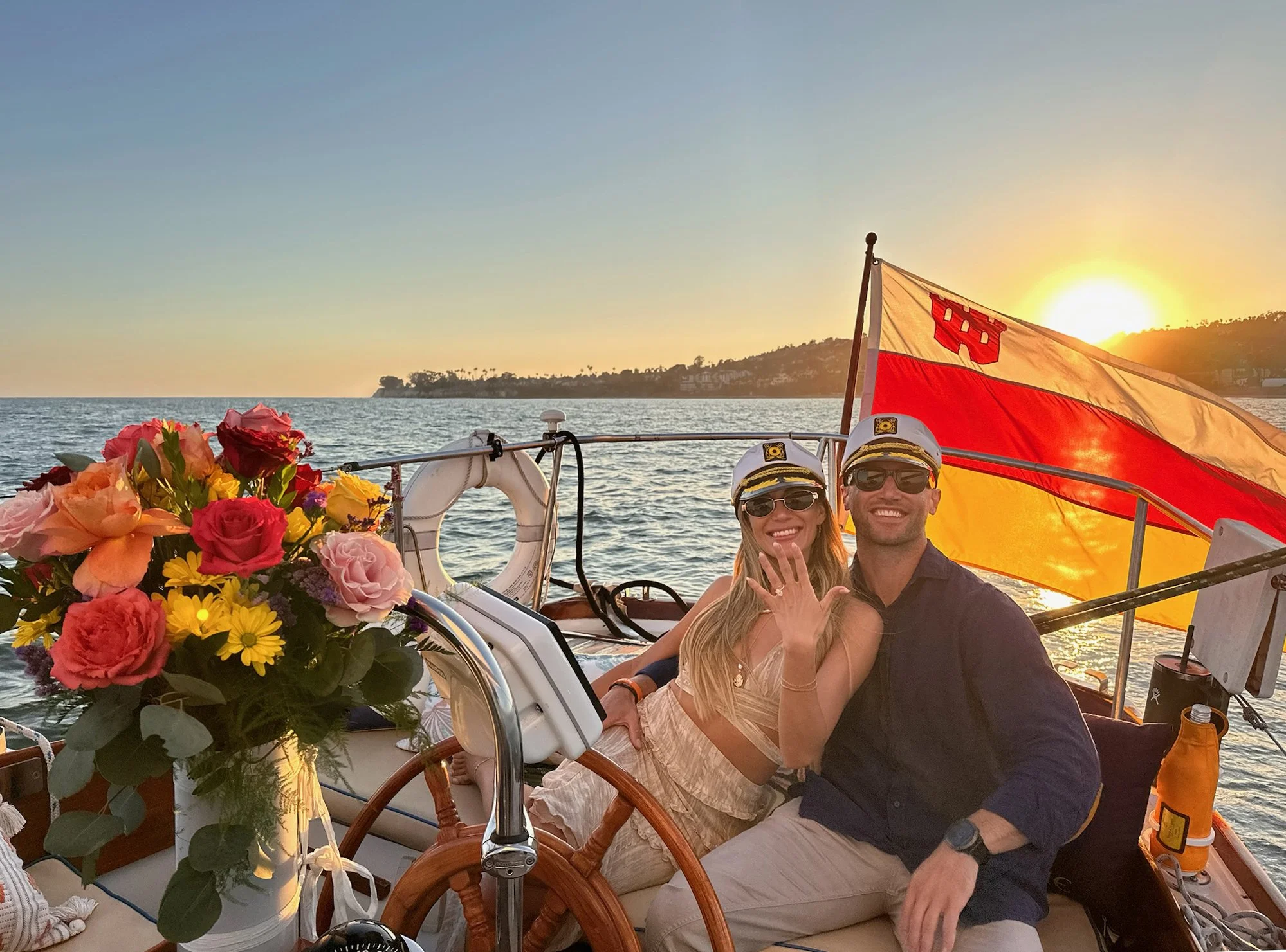 Couple celebrating their engagement aboard Yacht Kelpie with flowers and sunset over Santa Barbara.