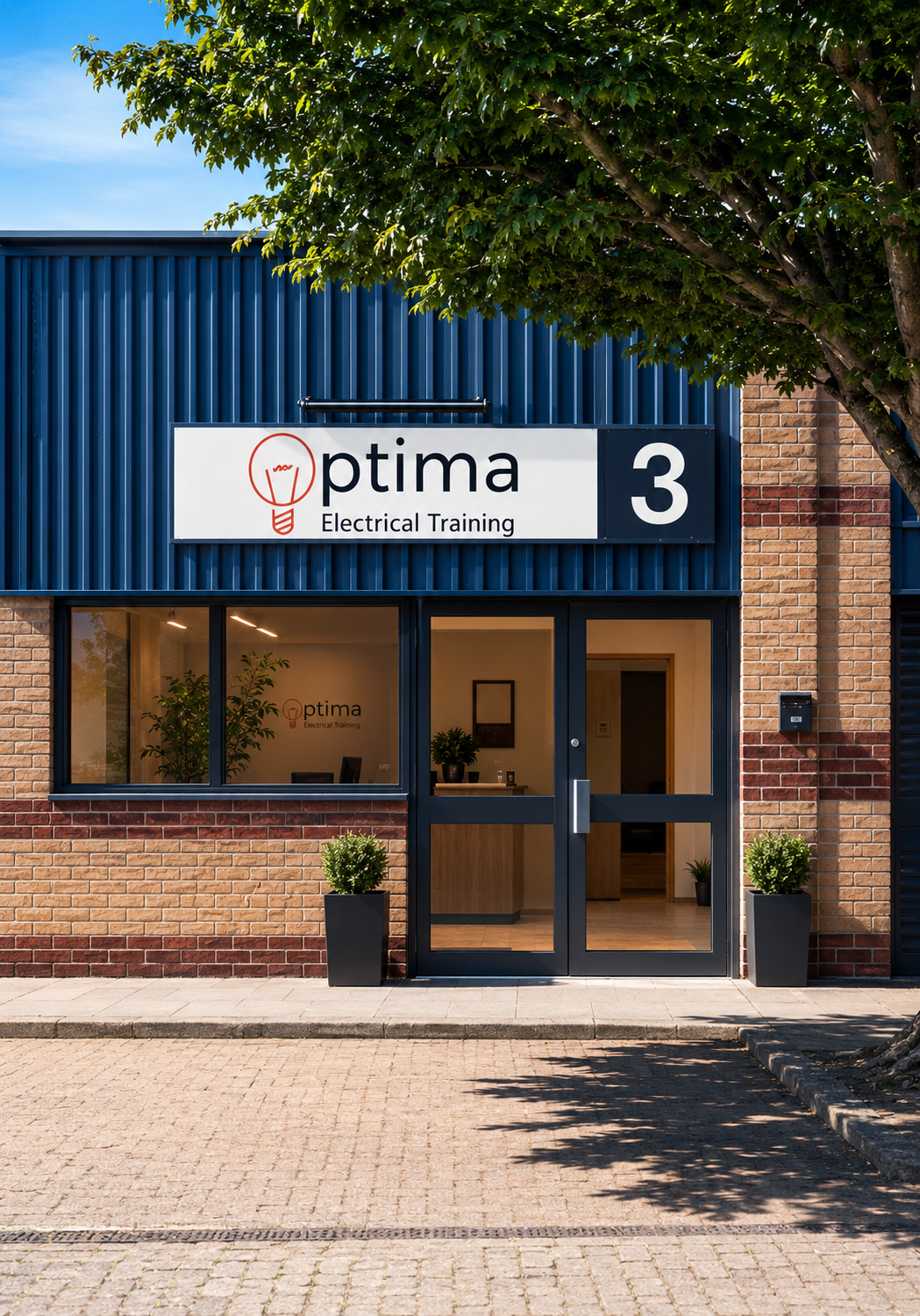 The exterior of a building with a blue corrugated metal upper section and a brick lower section. There are two windows on the upper part, a sign that reads 'optima Electrical Training 3,' and a black car parked on the left side. A green tree is partially in front of the building.
