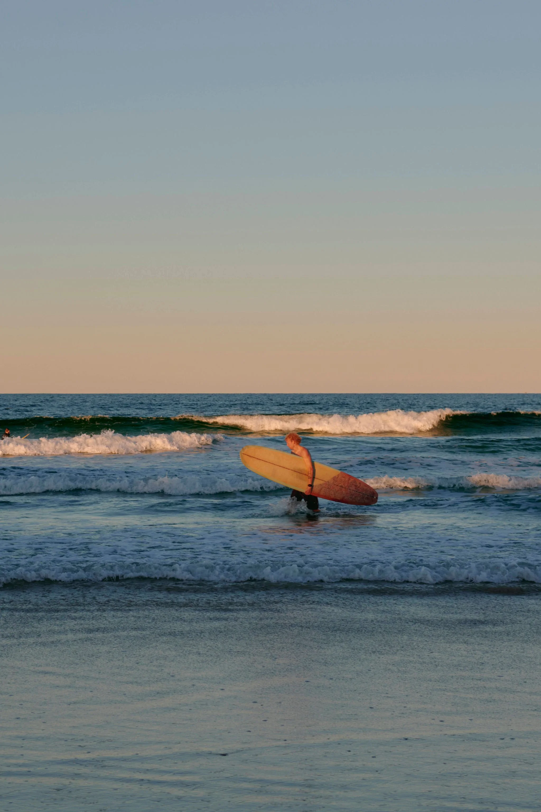 A yellow surfboard being launched into the air above the ocean waves during sunset or sunrise.