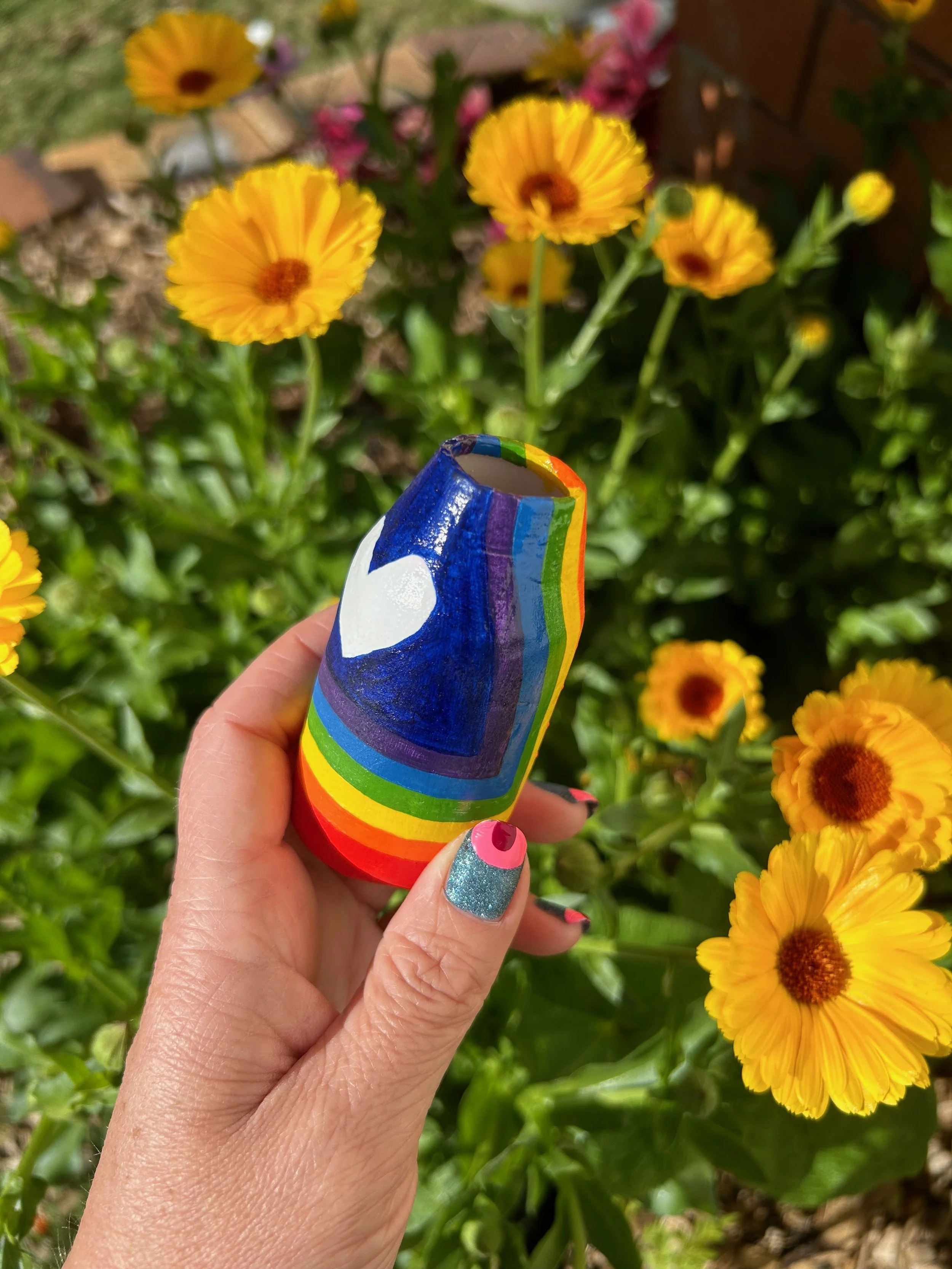 A hand is holding a little vase over bright yellow garden flowers.