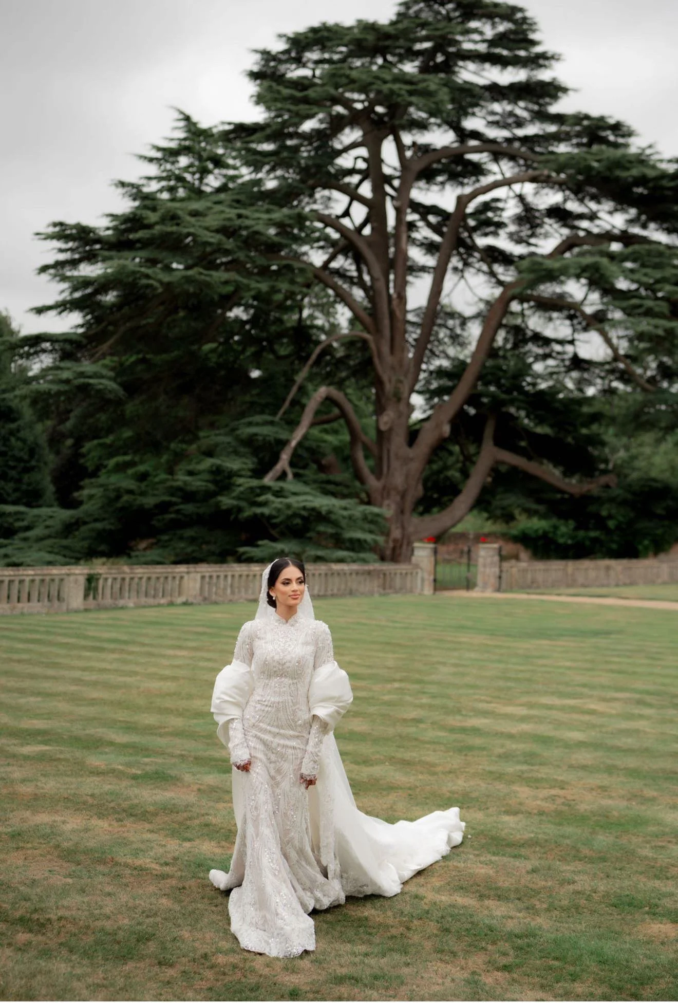 Bride holding embellished wedding dress, wearing veil and jewelry.