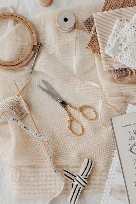 Sewing materials on beige fabric including scissors, measuring tape, thread spool, and bobbin.