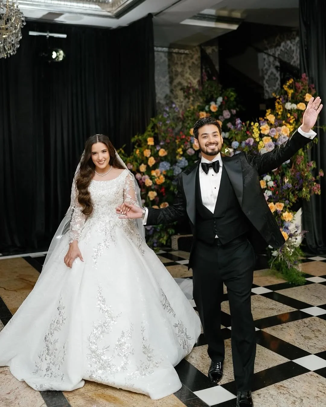 Bride holding embellished wedding dress, wearing veil and jewelry.