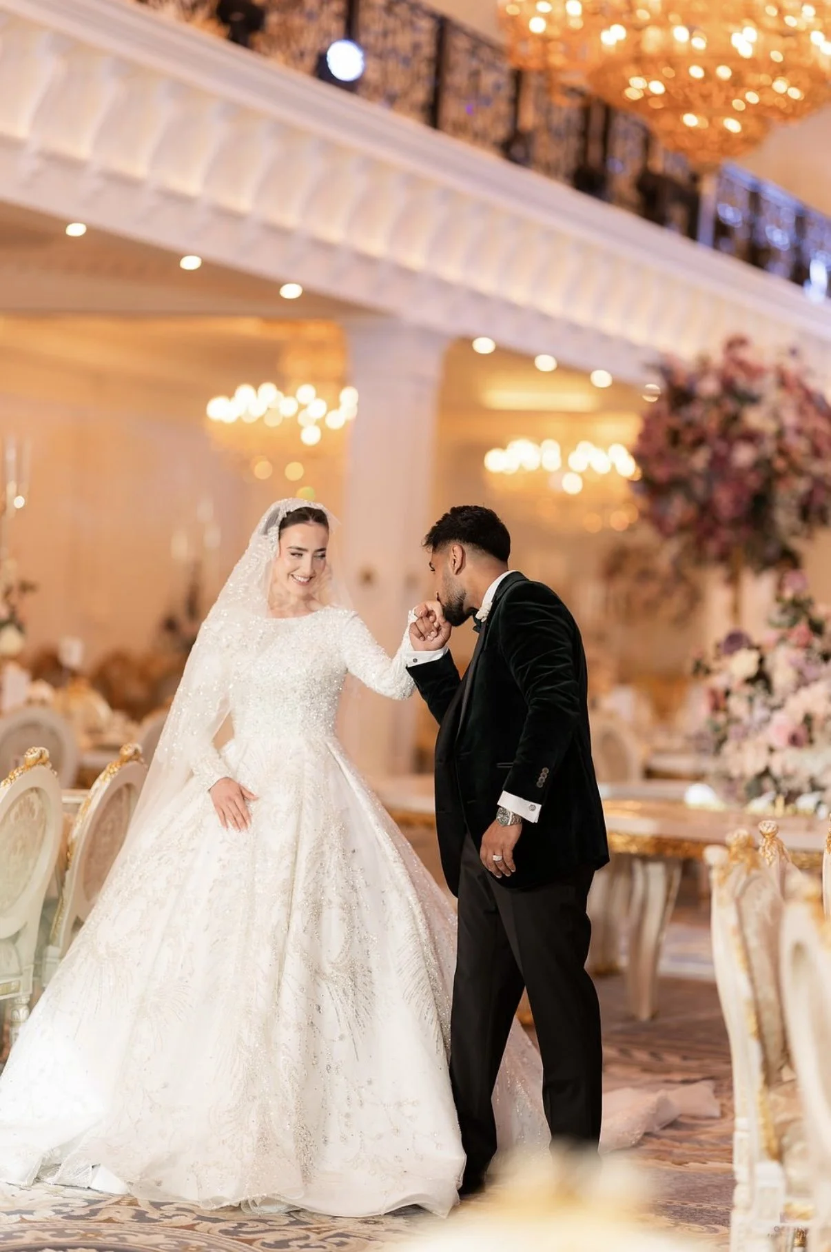 Bride holding embellished wedding dress, wearing veil and jewelry.
