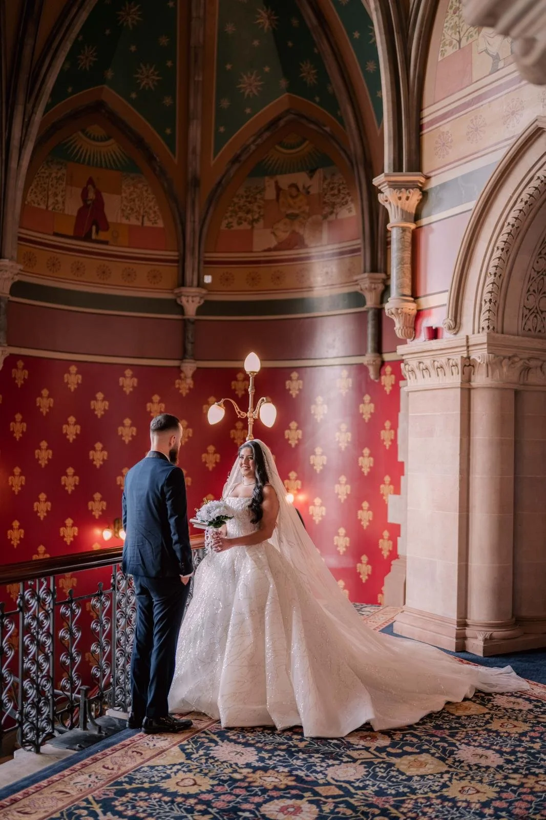 Bride holding embellished wedding dress, wearing veil and jewelry.