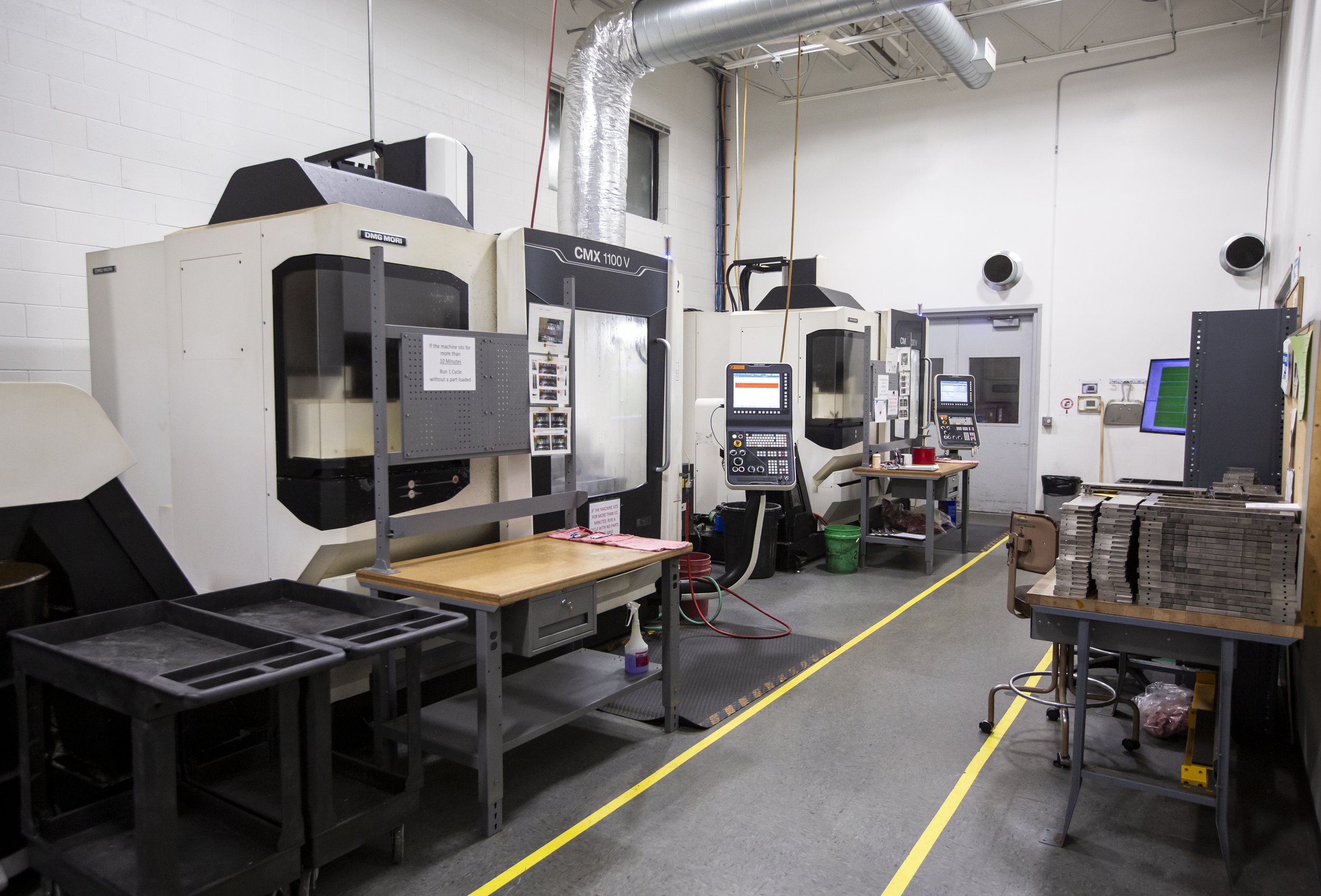 Industrial workshop with CNC machines, workstations, and metal sheets stacked on a table.
