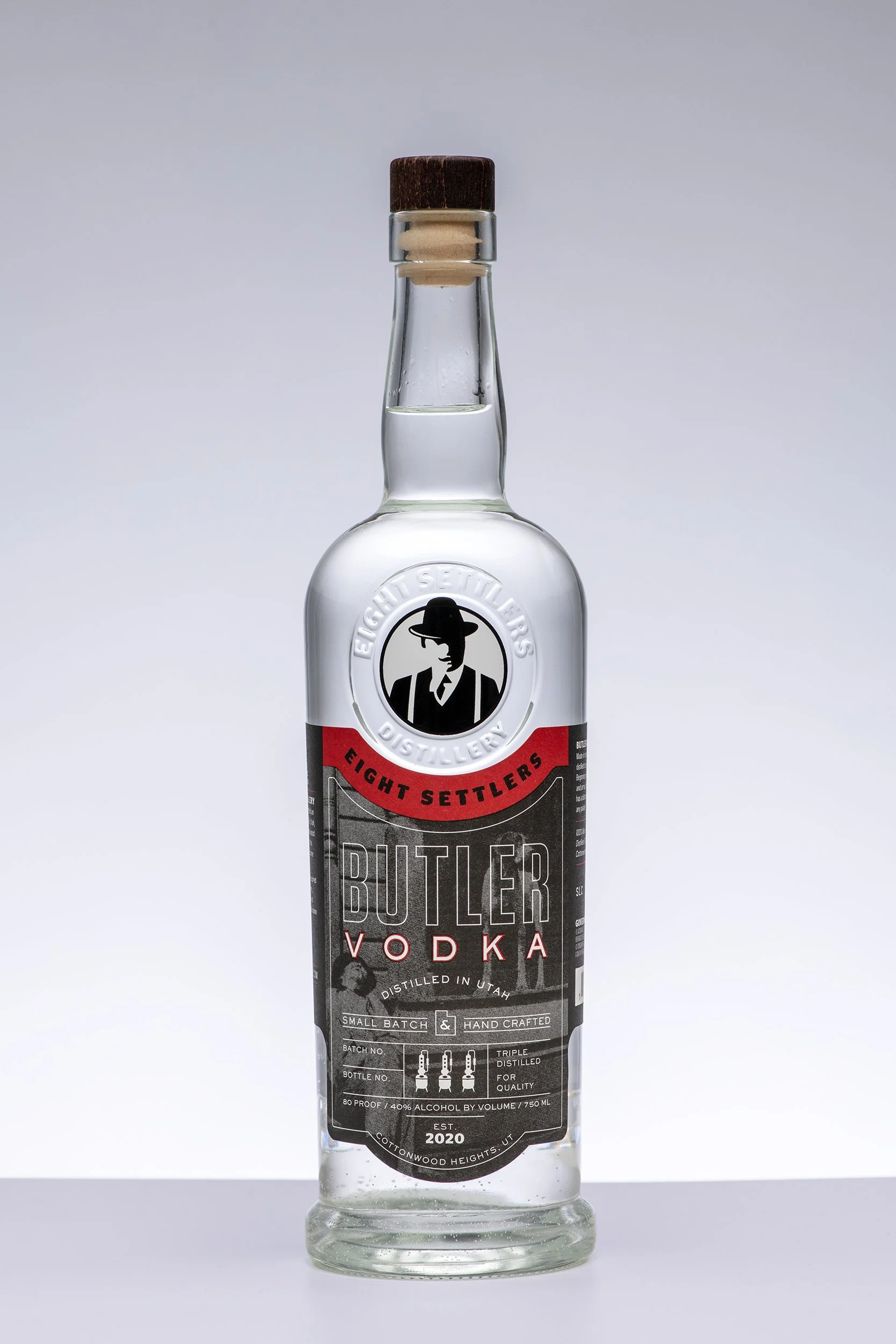 A clear glass bottle of Butler vodka with a black and red label, featuring a man in a hat and a suit, and a black cap.