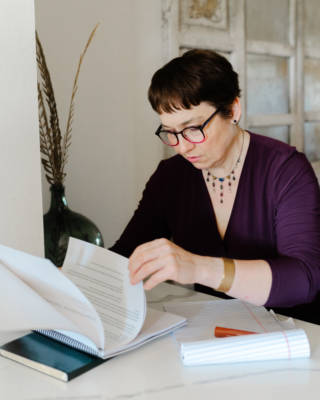 Elizabeth Menes, Director of Story for Kwedar & Co., reviewing written notes at a desk, reflecting on leadership storytelling and moving beyond a traditional elevator pitch