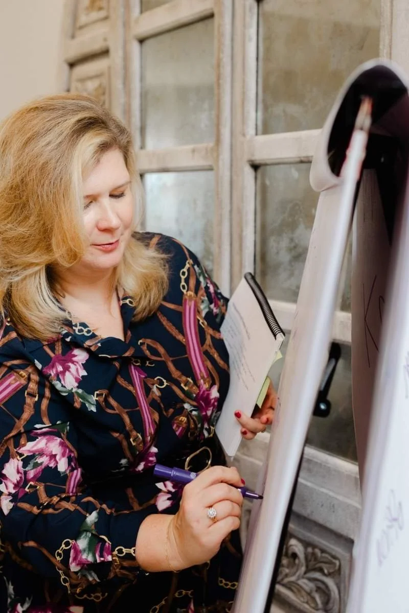 Lauren Kwedar Cockerell, President of Kwedar & Co., outlining strategy on a whiteboard while holding notes, illustrating a hands-on approach to PR and marketing planning