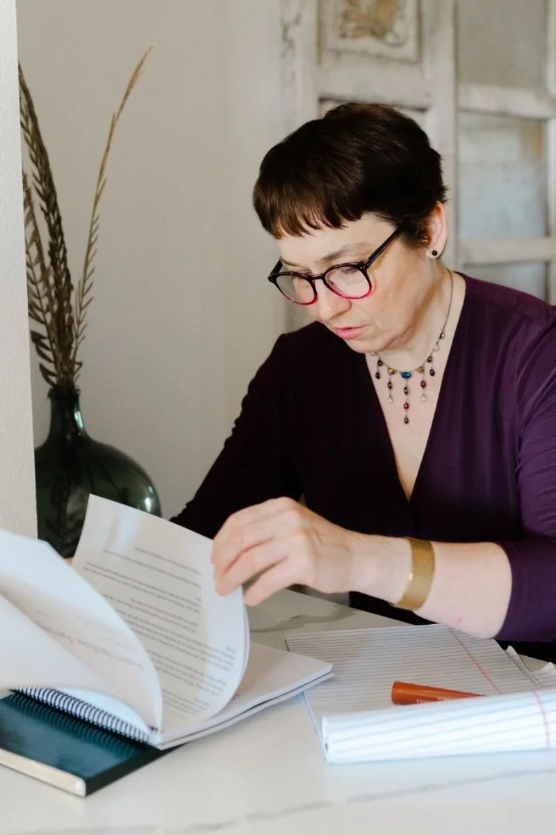 Elizabeth Menes, Director of Story for Kwedar & Co., reviewing printed documents and notes at a desk, focused on refining clear and thoughtful client messaging