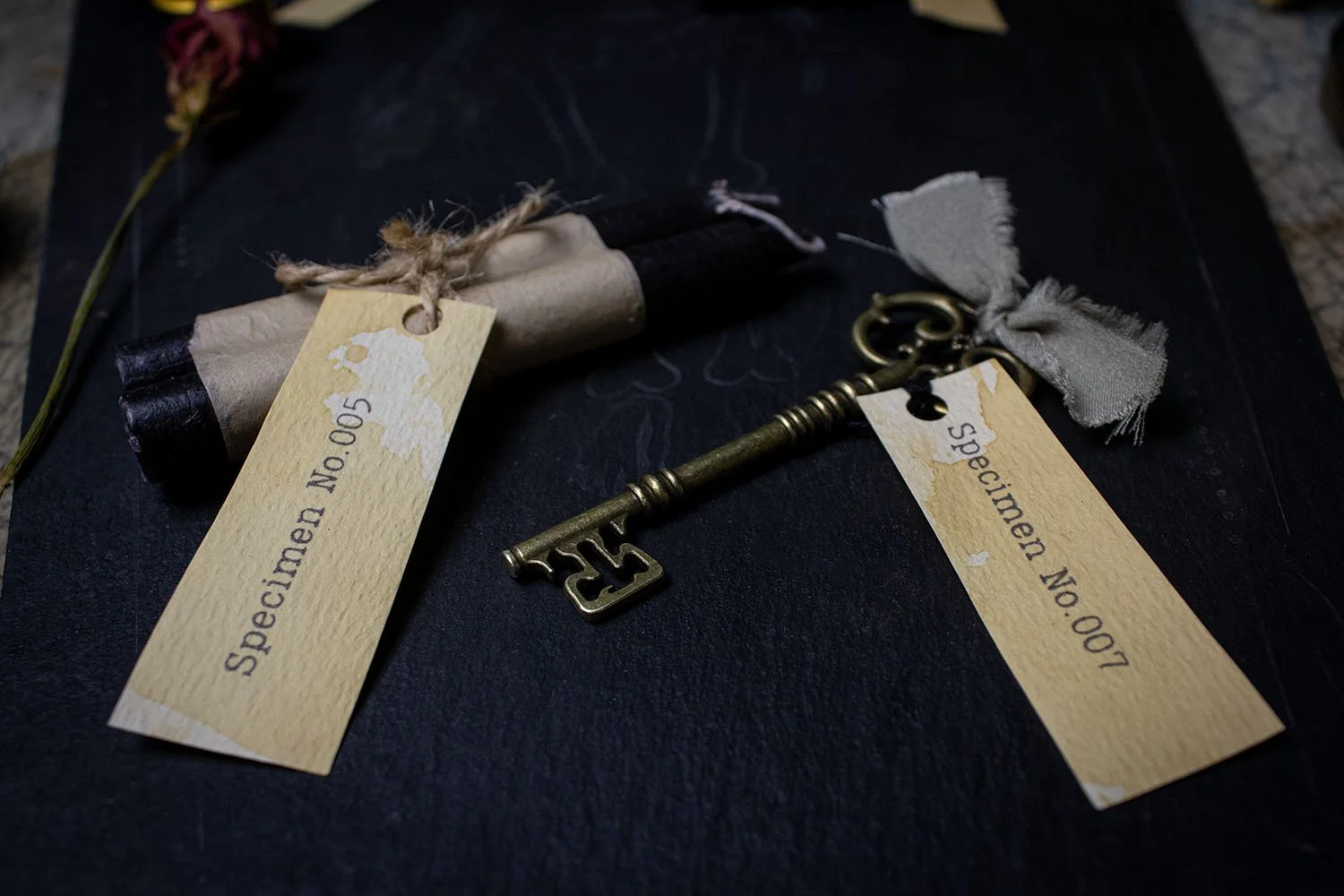 A vintage brass key tied with a beige ribbon, alongside a wrapped bundle with a 'Specialen No.005' label, on a dark surface.