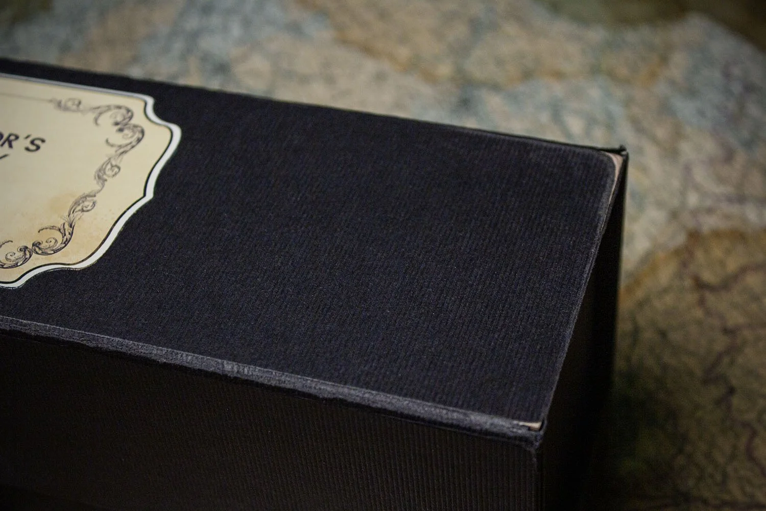 Close-up of a black textured box with a decorative label on the top corner.