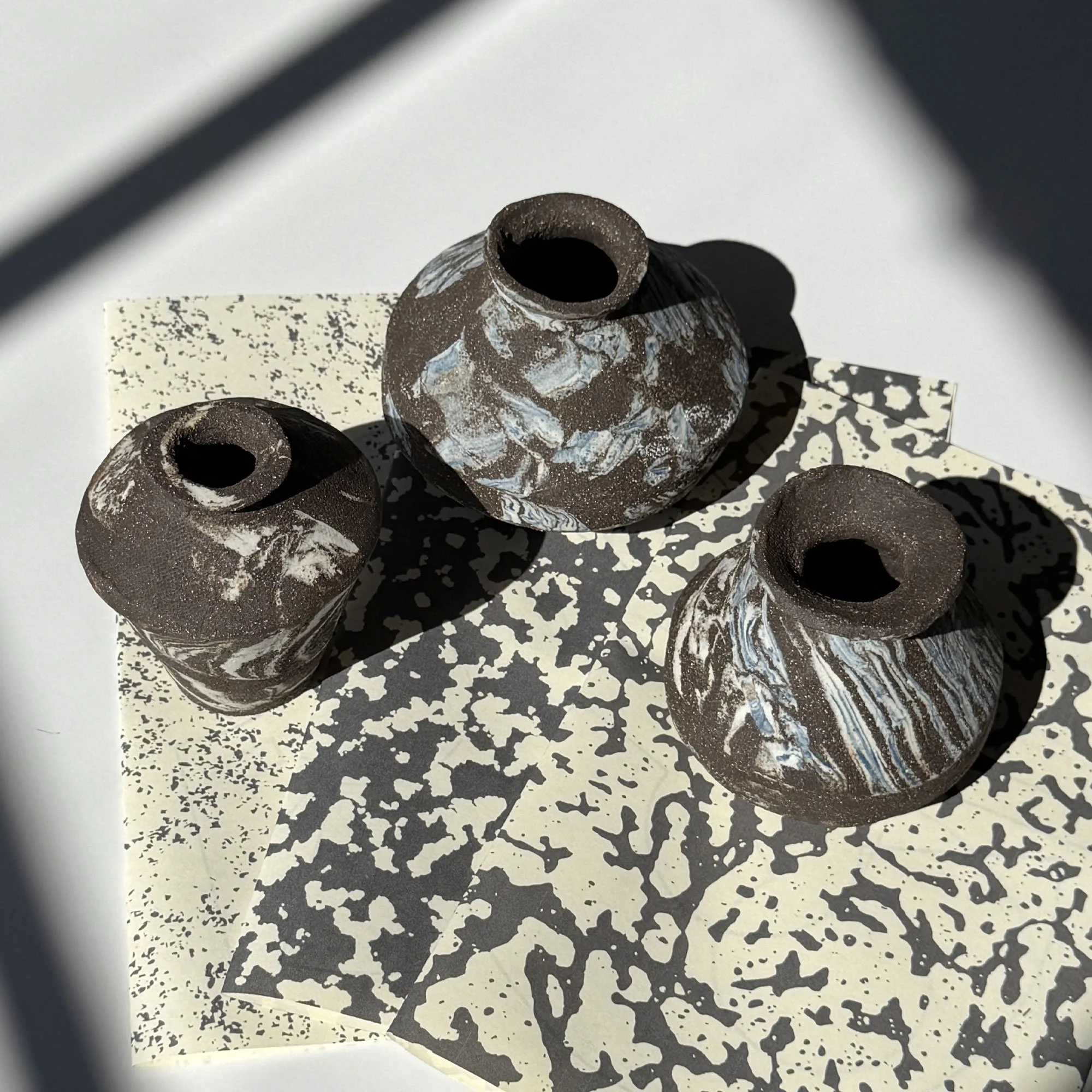 Three Canto cacharritos vessels built from slab templates, marbled clay, overhead view on patterned paper