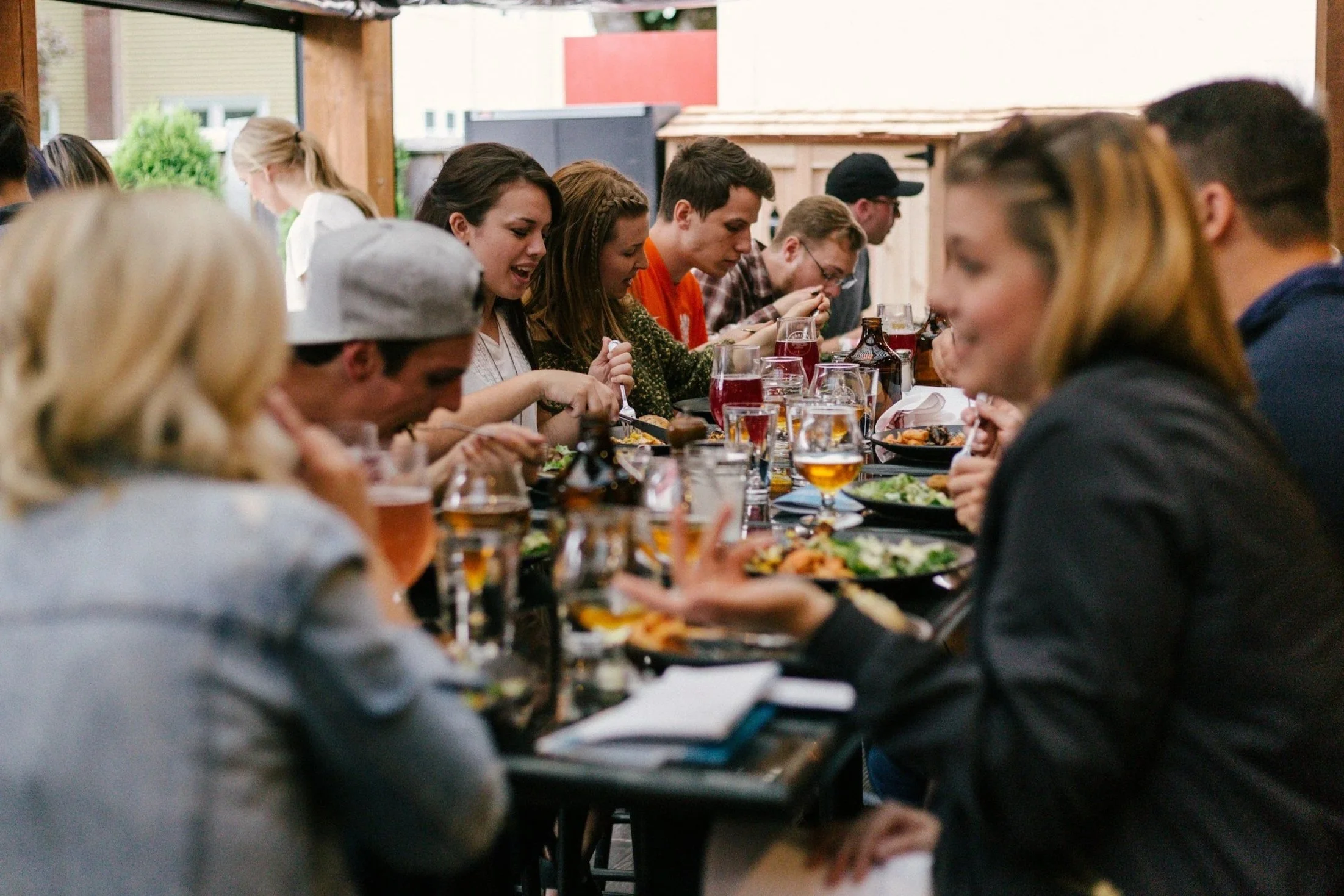 A group of people eating and talking around a long restaurant table filled with plates and drinks.