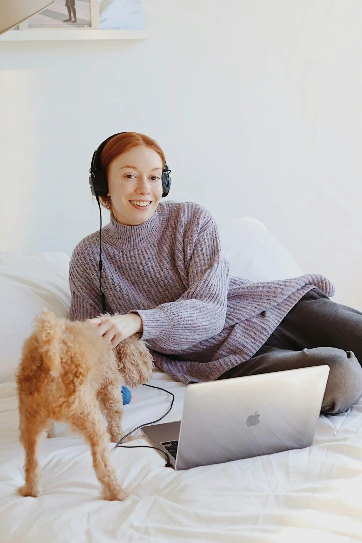 Person smiling while working from home on a laptop with a dog nearby, representing a comfortable and supportive remote work environment.