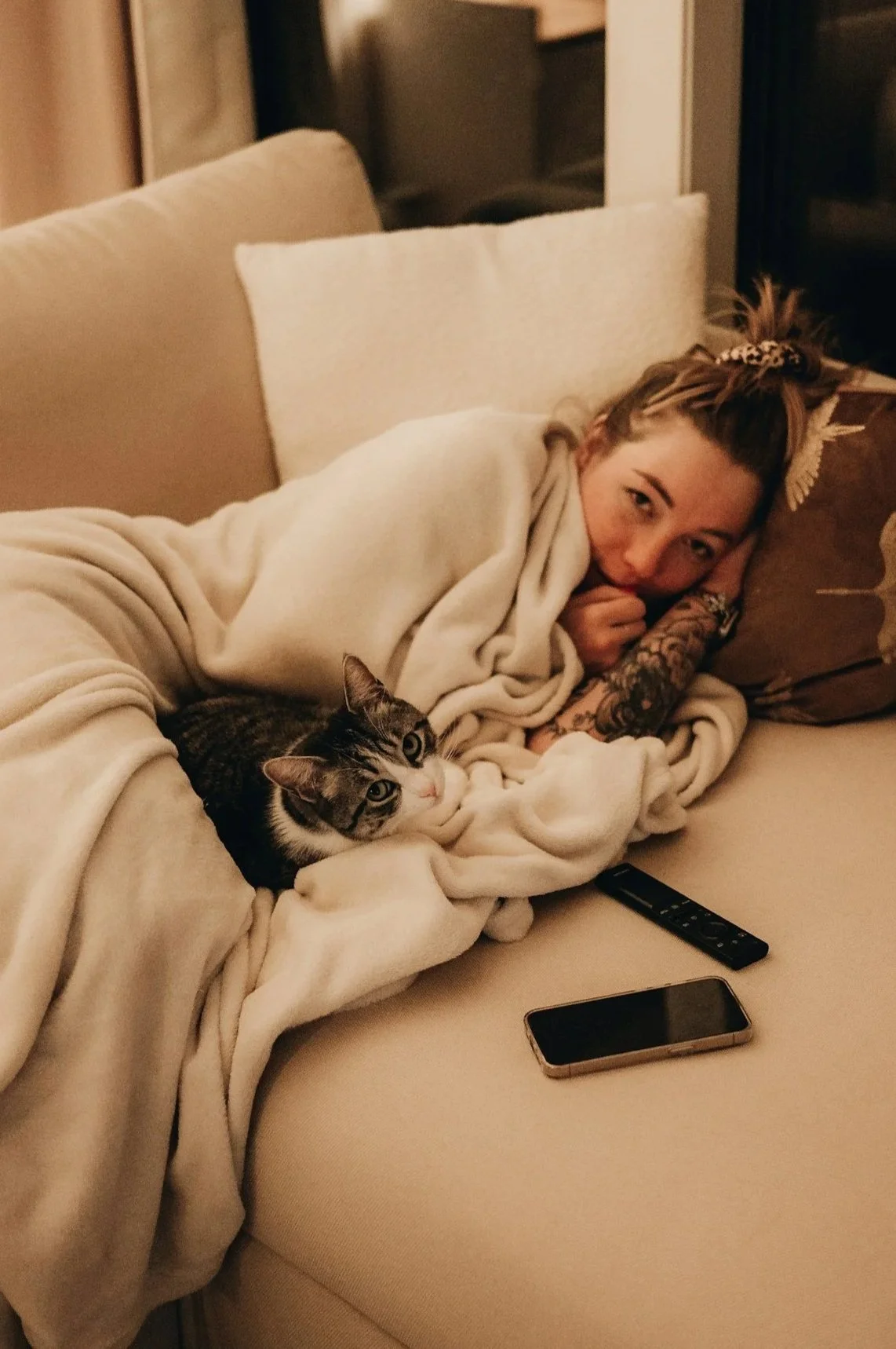 woman laying on a couch with a blanket and cat too exhausted to attend funeral
