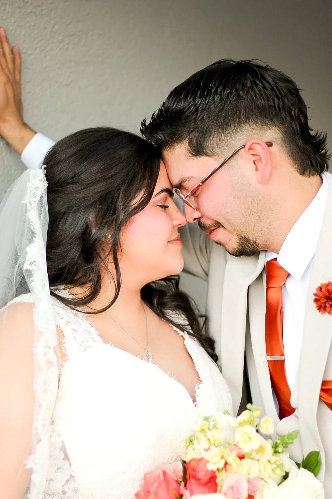 A bride and groom are touching foreheads and smiling, with eyes closed, during a wedding celebration.