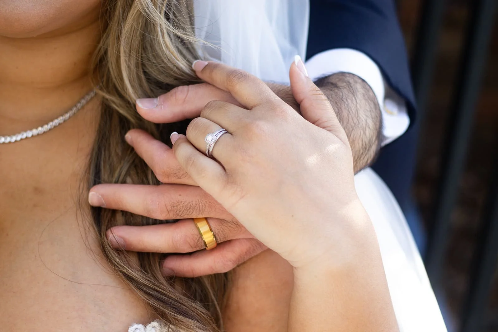 Close-up of a couple's hands showing wedding rings, with the woman's hand resting on the man's chest and their bodies close together.