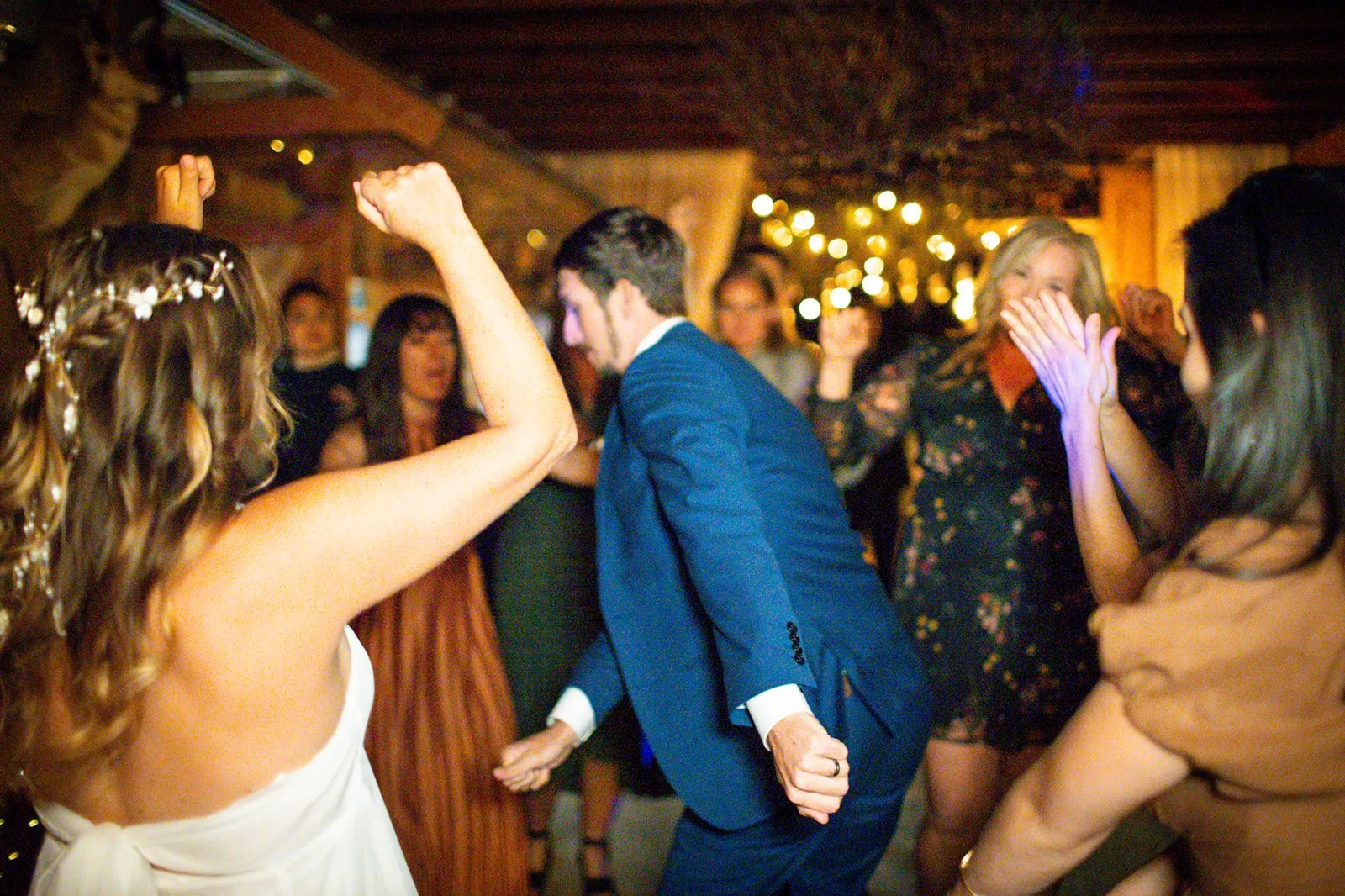 People dancing and celebrating at a party or wedding reception in a warmly lit room.